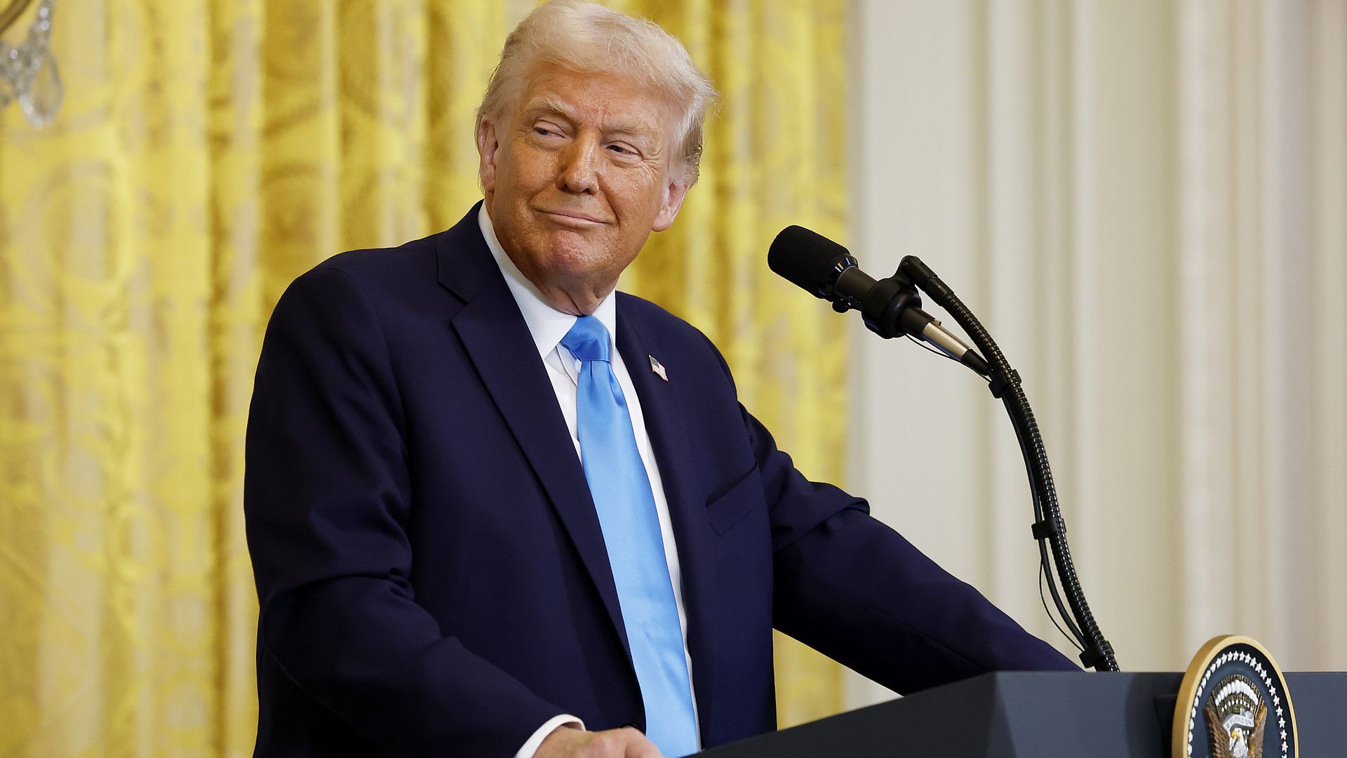 Trump in suit with light blue tie and gold curtain background