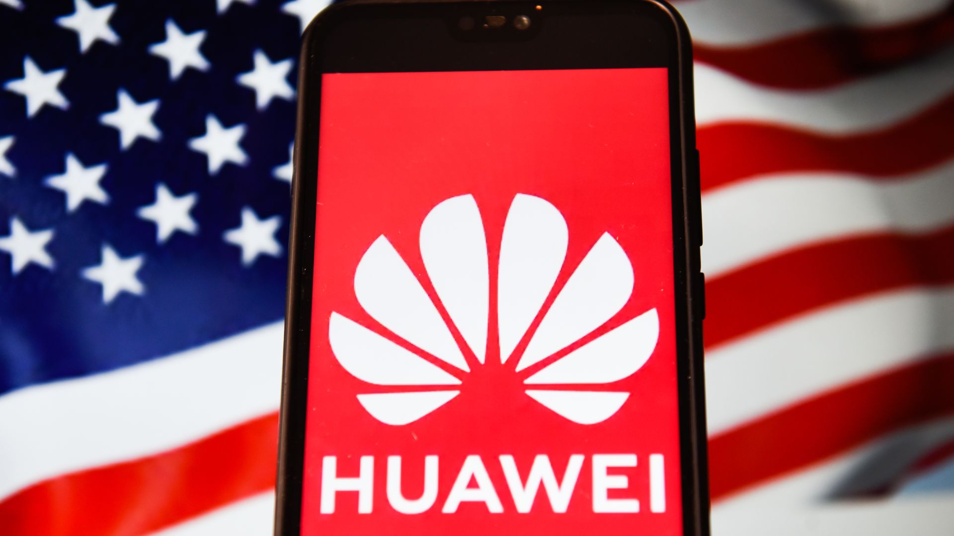 This photo shows the Huawei logo displayed on a phone with the American flag in the background.