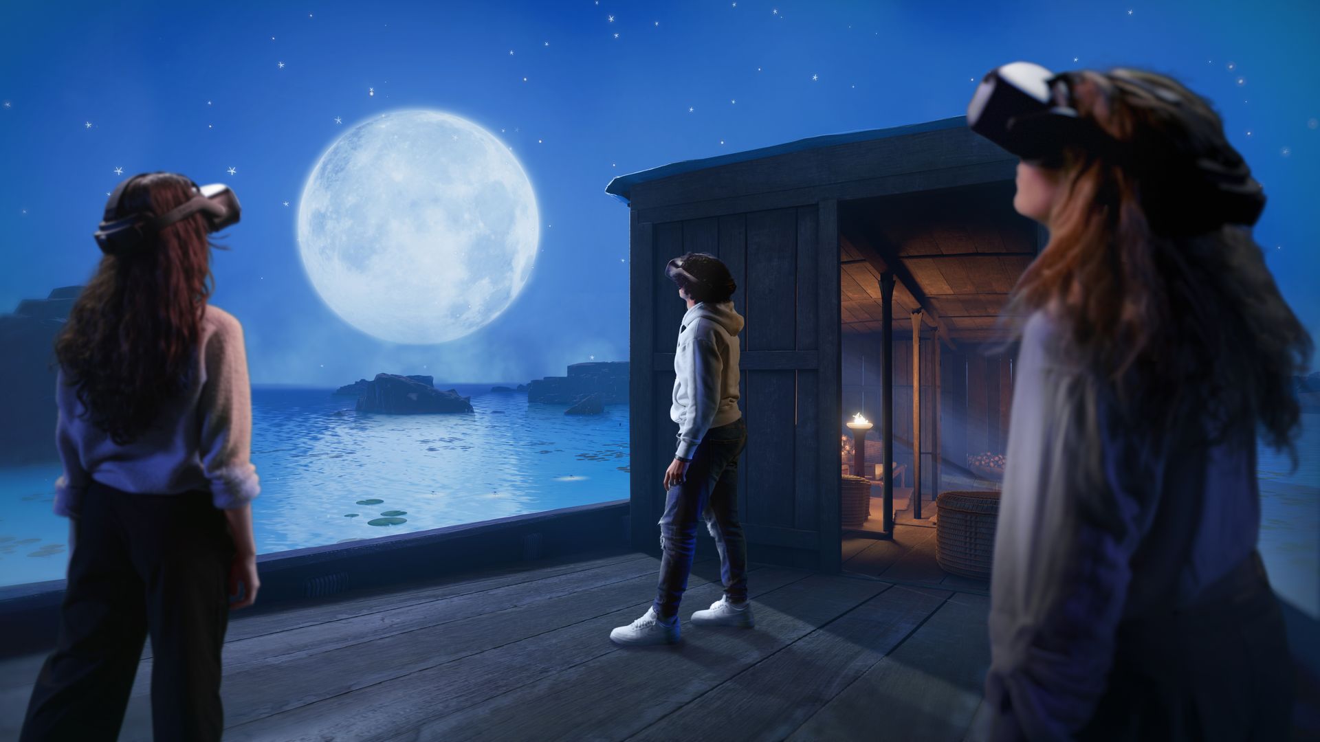 Three people wearing virtual reality headsets stand on a wooden deck beside water under a starry night sky with a large full moon and rocky outcrops in the distance.