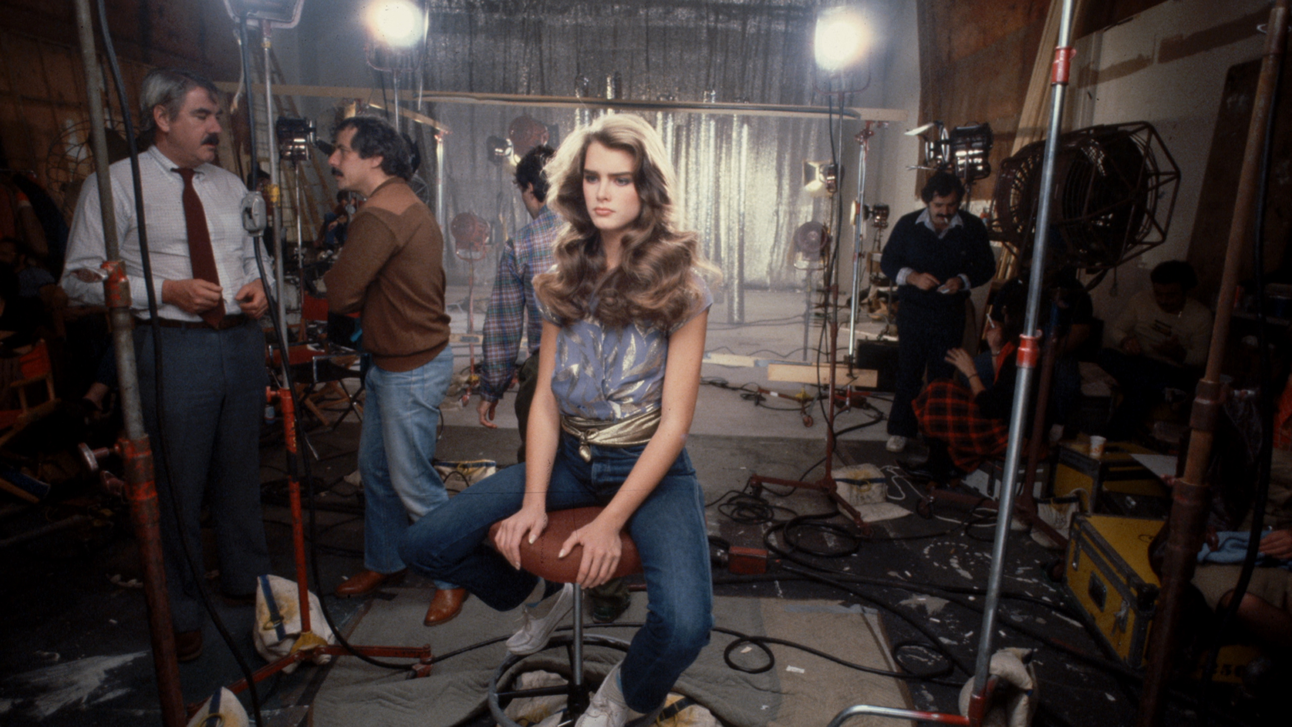 A younger Brooke Shields sitting on a stool with a blank stare.