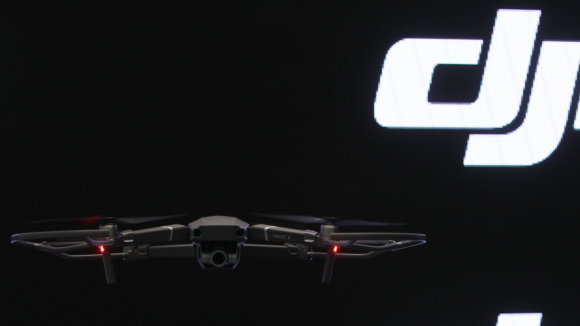 A DJI drone hovering in front of a background with the DJI logo