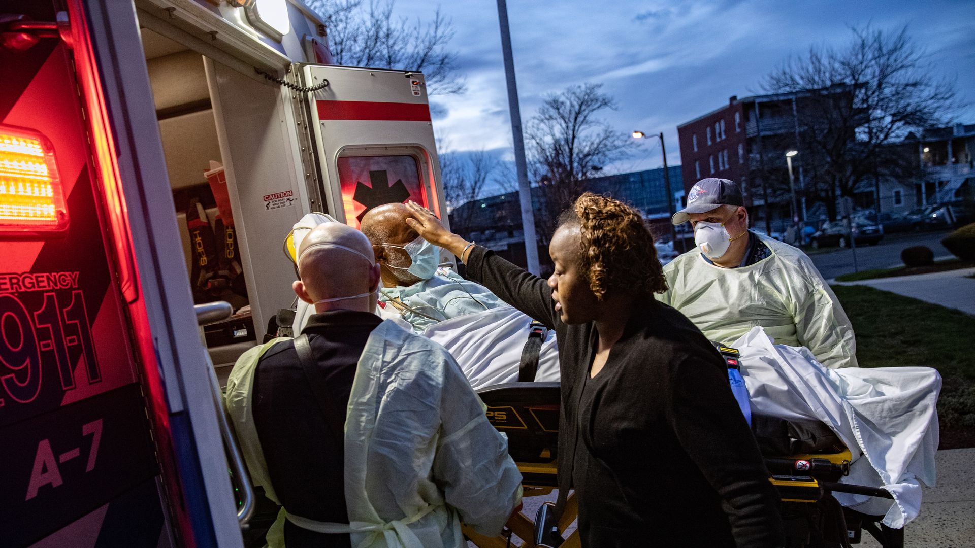 In this image, a woman touches a mans' head as he is carried into an ambulance on a stretcher