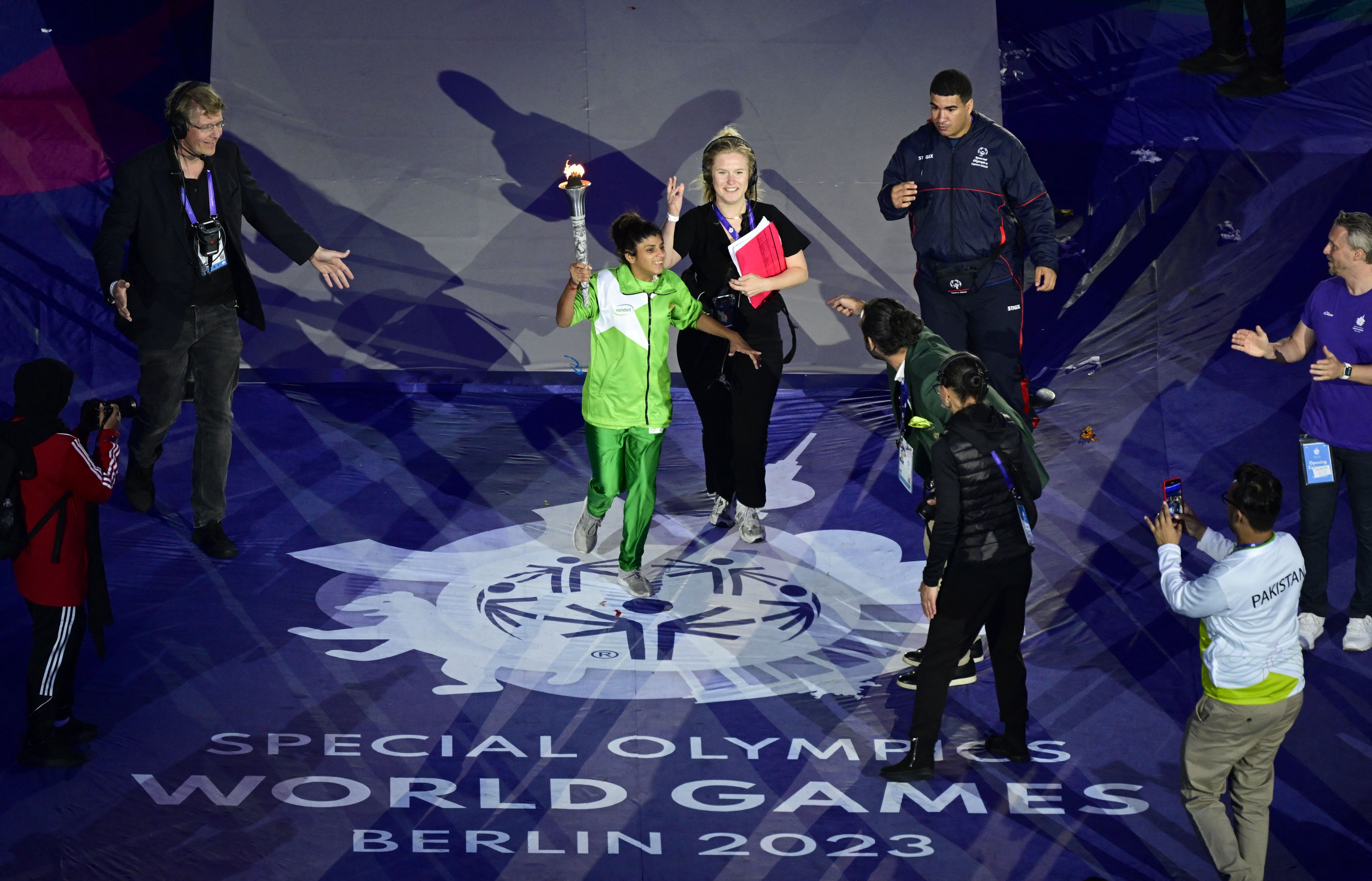 An athlete is coached as she carries the flame around the stadium during the opening ceremony of the Special Olympics World Games.