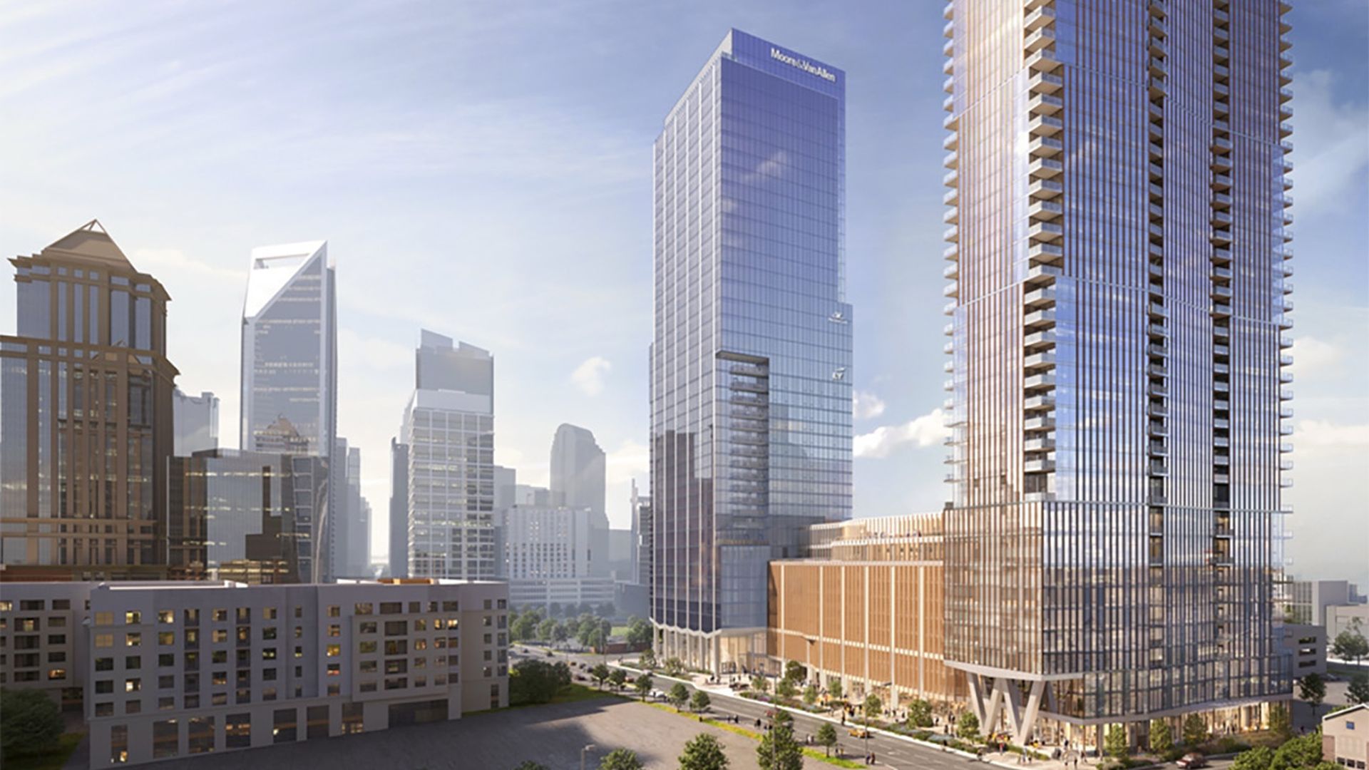 Cityscape with modern high-rise glass buildings under a partly cloudy blue sky, featuring a tall reflective building and a distinctive angled skyscraper in the background.