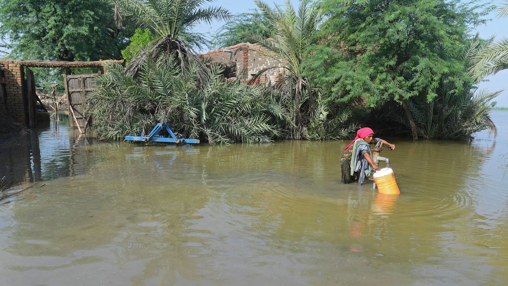A flood affected woman fills drinking water from a partially submerged handpump 