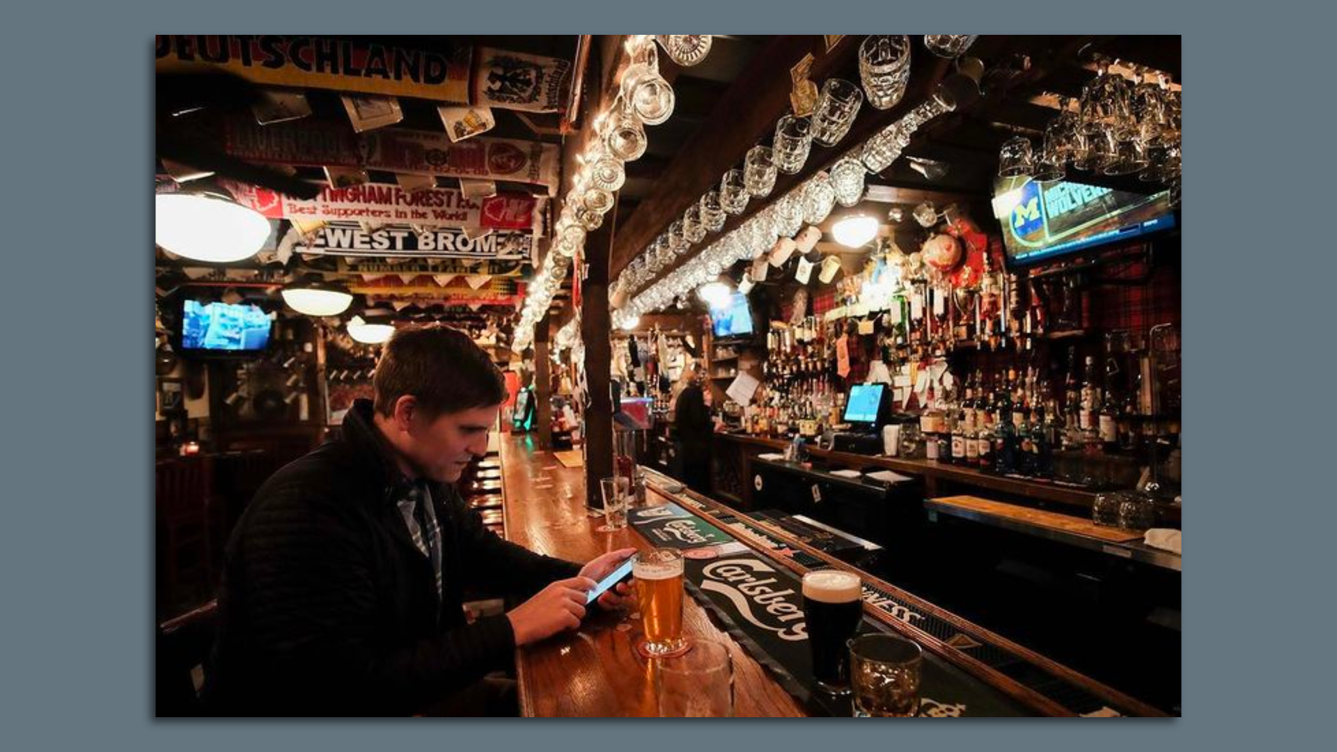 A frustrated-looking man sits at the bar of a restaurant drinking a beer. 