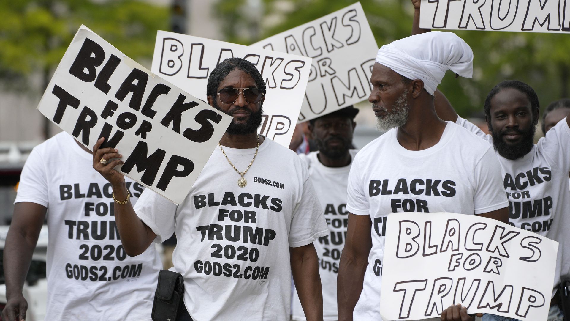 Black supporters of Trump wear shirts that say "Blacks for Trump 2020" and carry signs.