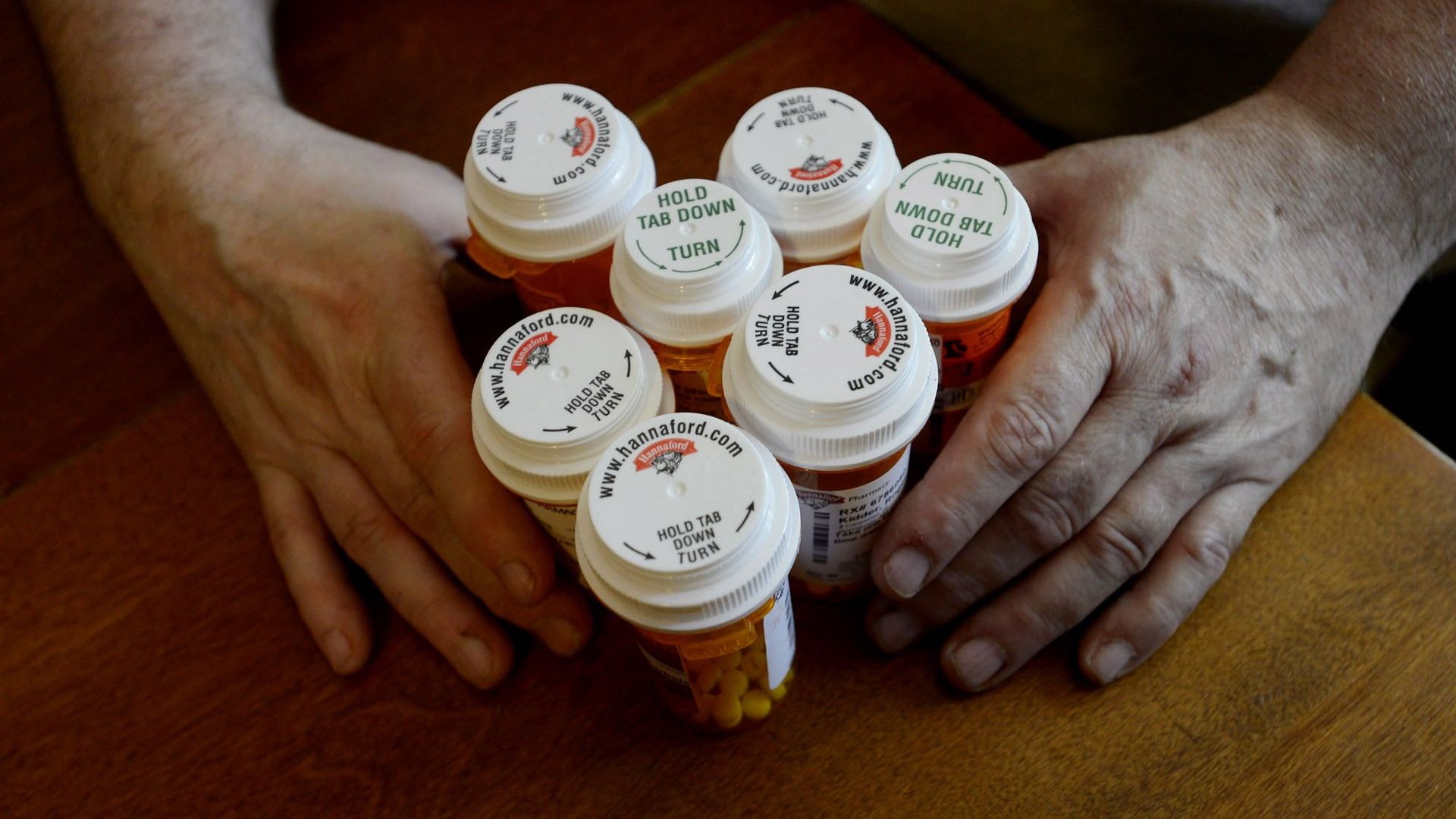 A person holds seven bottles of prescription drugs.