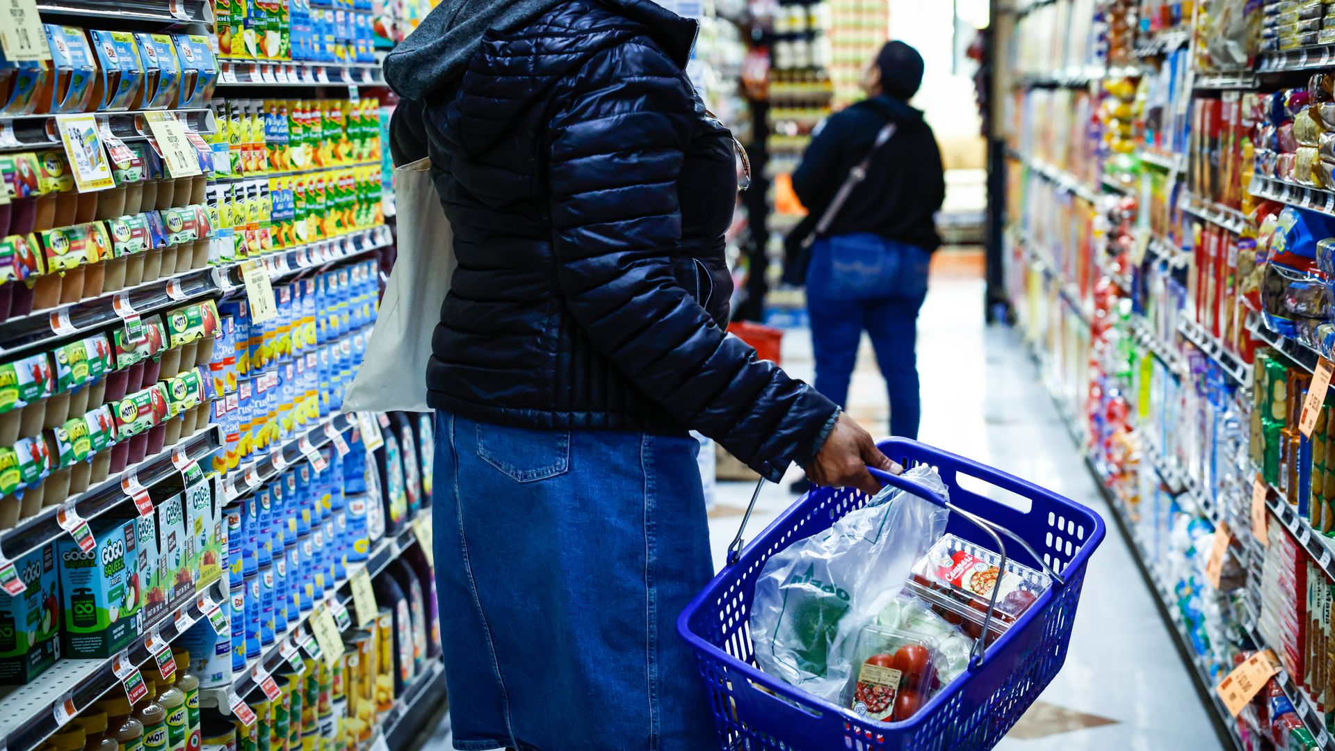A shopper fills a blue wicker basket with groceries. 