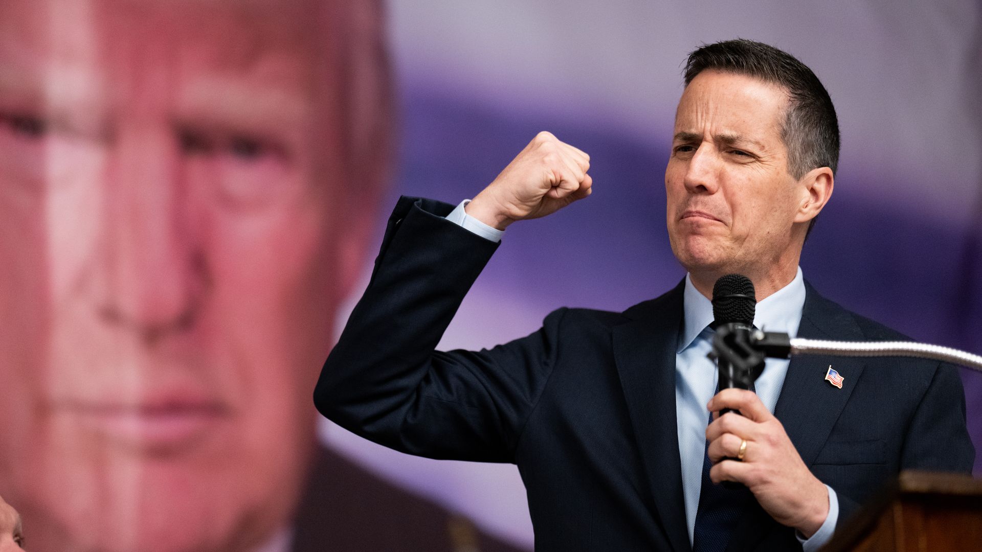 Bernie Moreno pumping his fist with an image of Donald Trump's face in the background