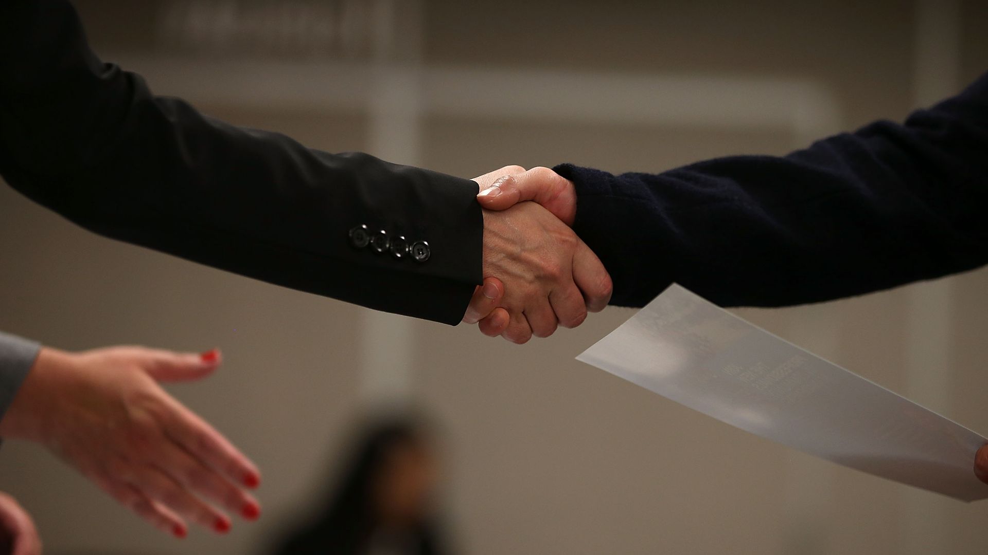 Hands shake and exchange a resume.