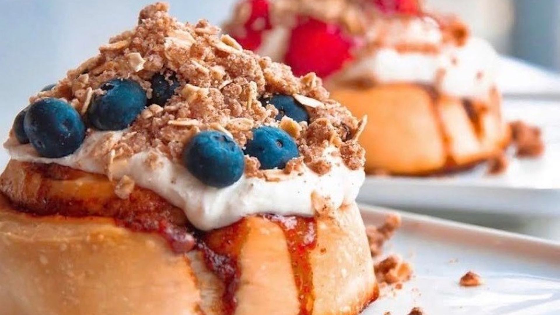 Two cinnamon rolls topped with creamy frostings and fruit.