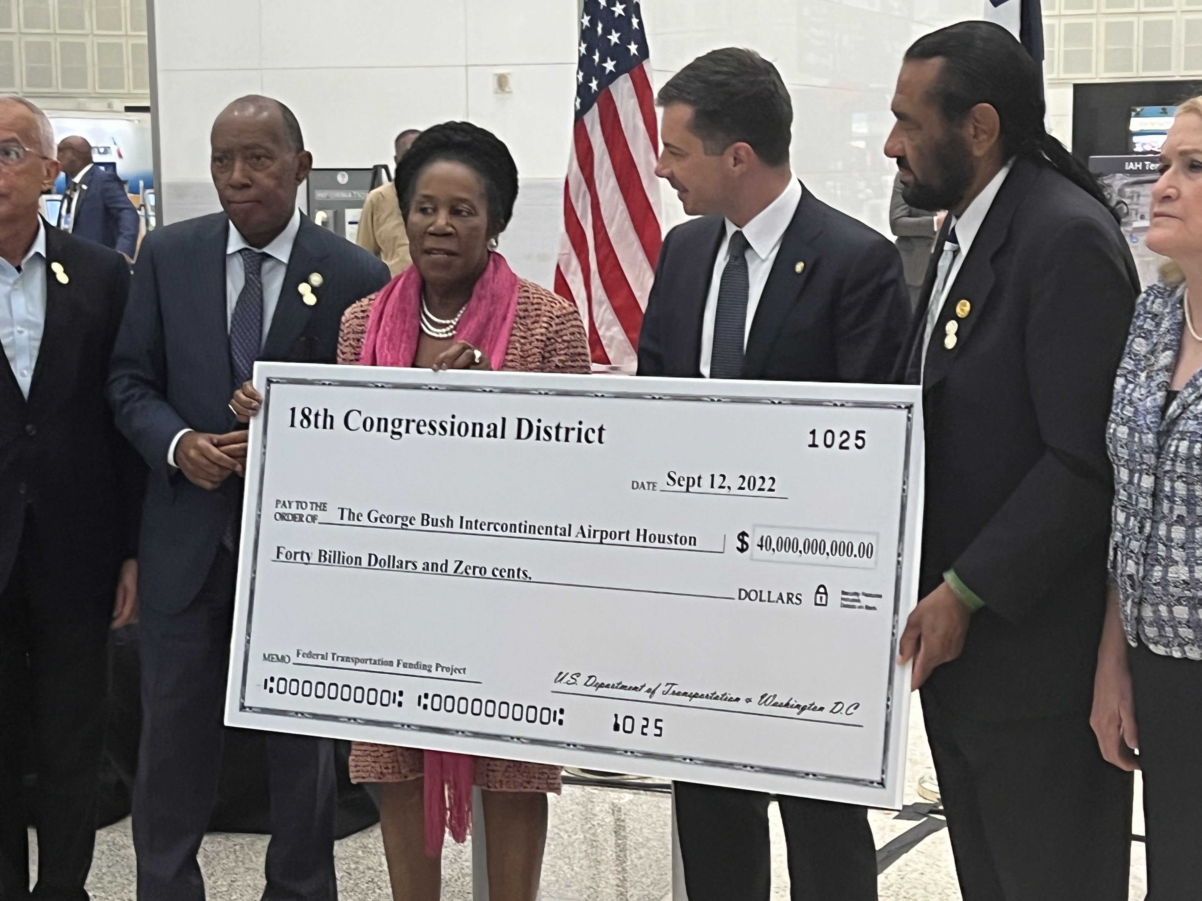Mayor Sylvester Turner, U.S. Rep. Sheila Jackson Lee and Transportation Secretary Pete Butigieg hold a giant check in front of an American flag