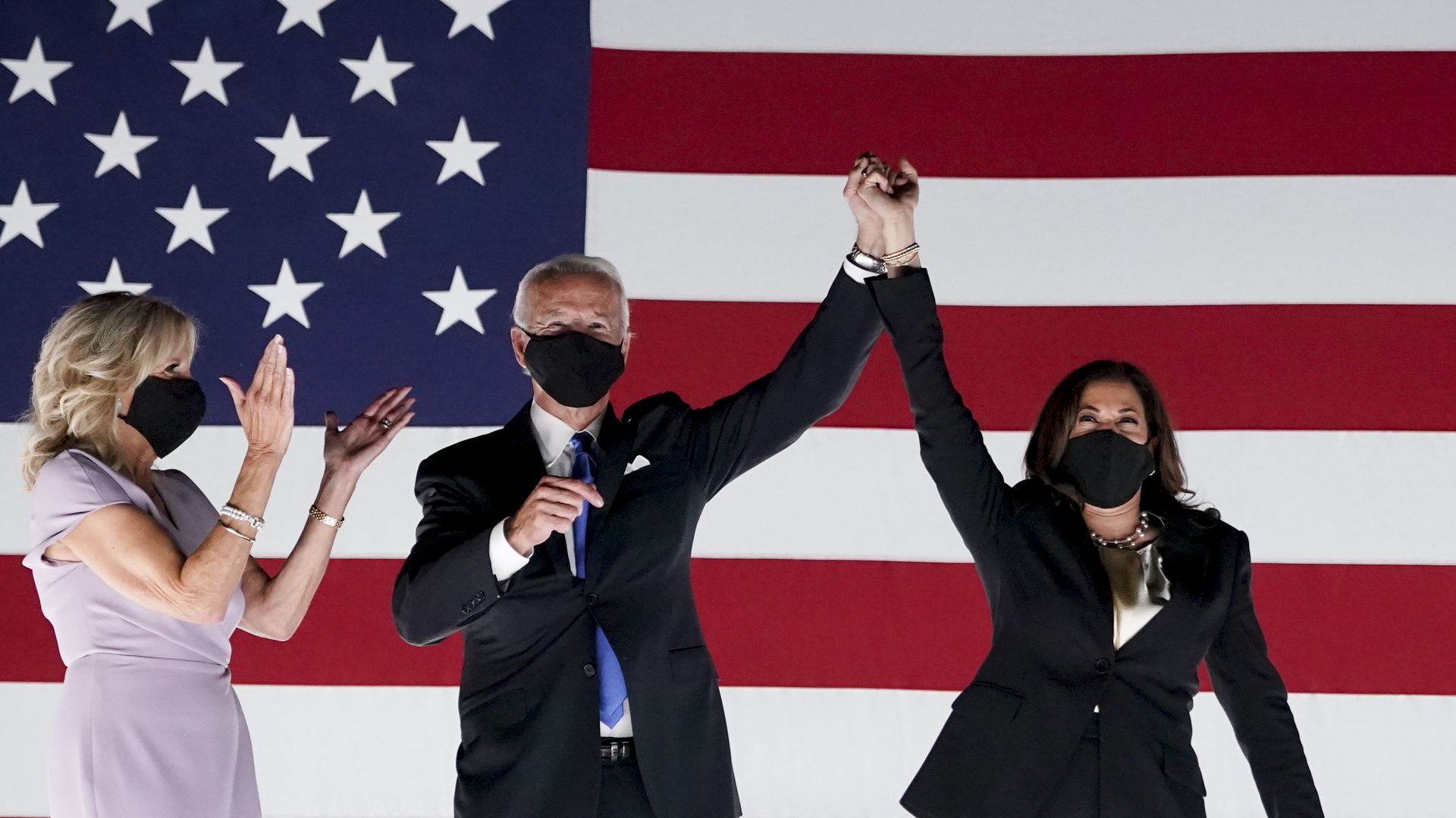 Jill Biden, Joe Biden and Kamala Harris, wearing masks, in front of a U.S. flag.