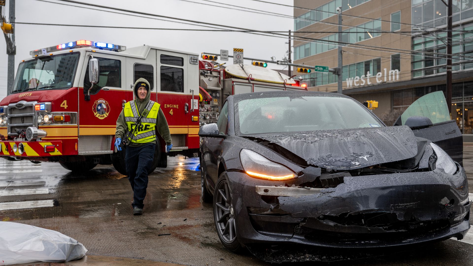 A first responder responds to a crash. A fire truck is in the background and a smashed up sedan is in the foreground.