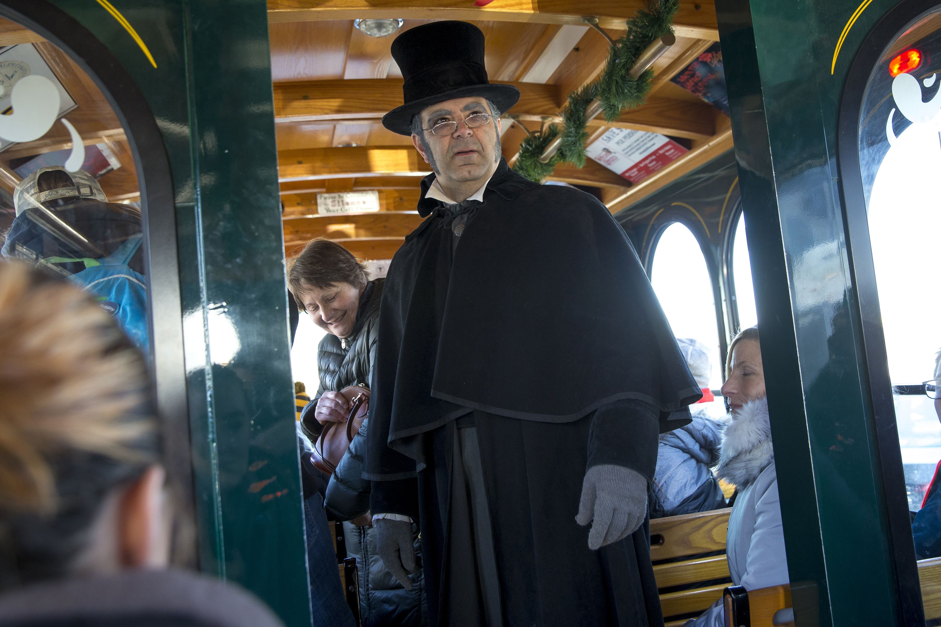 A man dressed as Scrooge, in black cape and top hat, standing in a trolley.