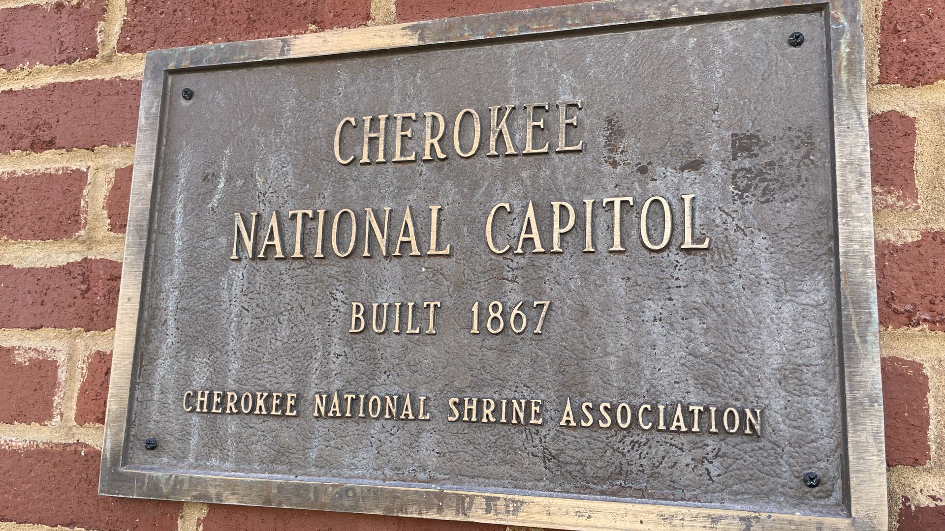 A sign marks the capitol of the Cherokee Nation is shown on a brick wall.