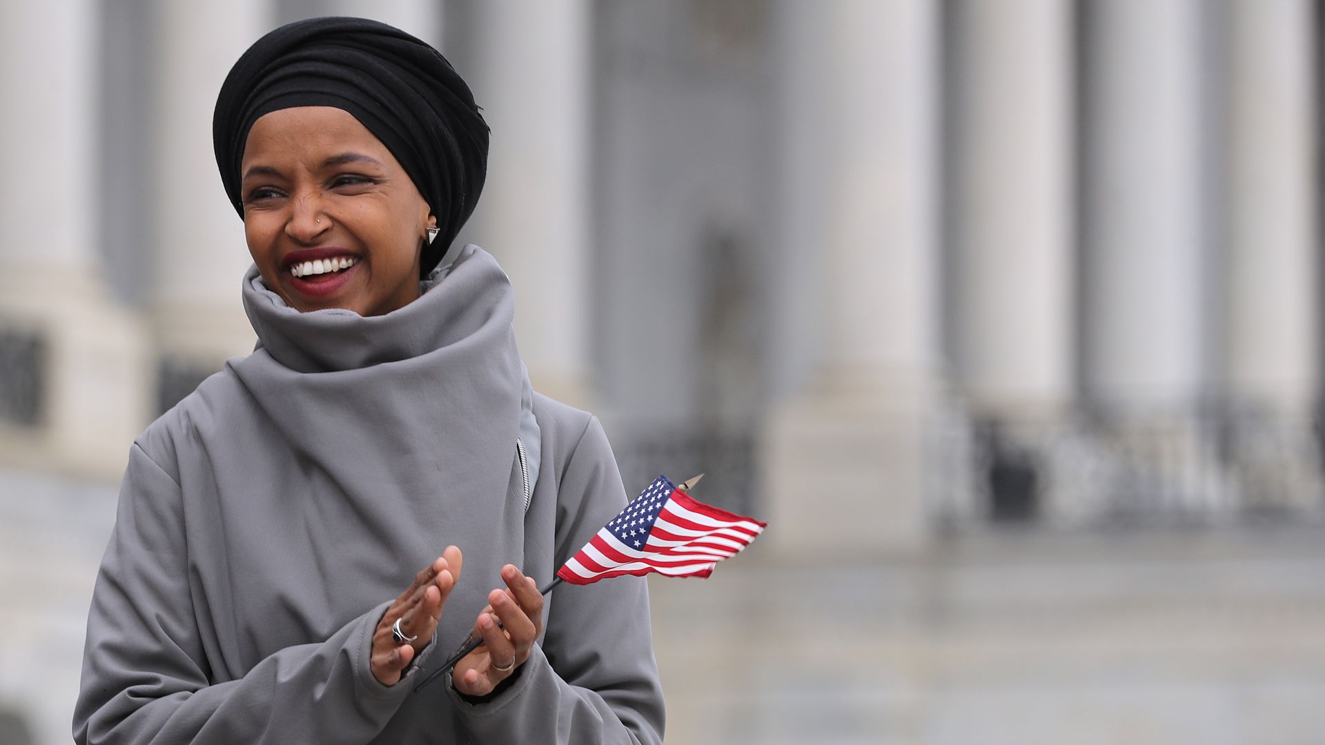 In this image, Rep. Omar holds a small American flag in one hand while clapping.