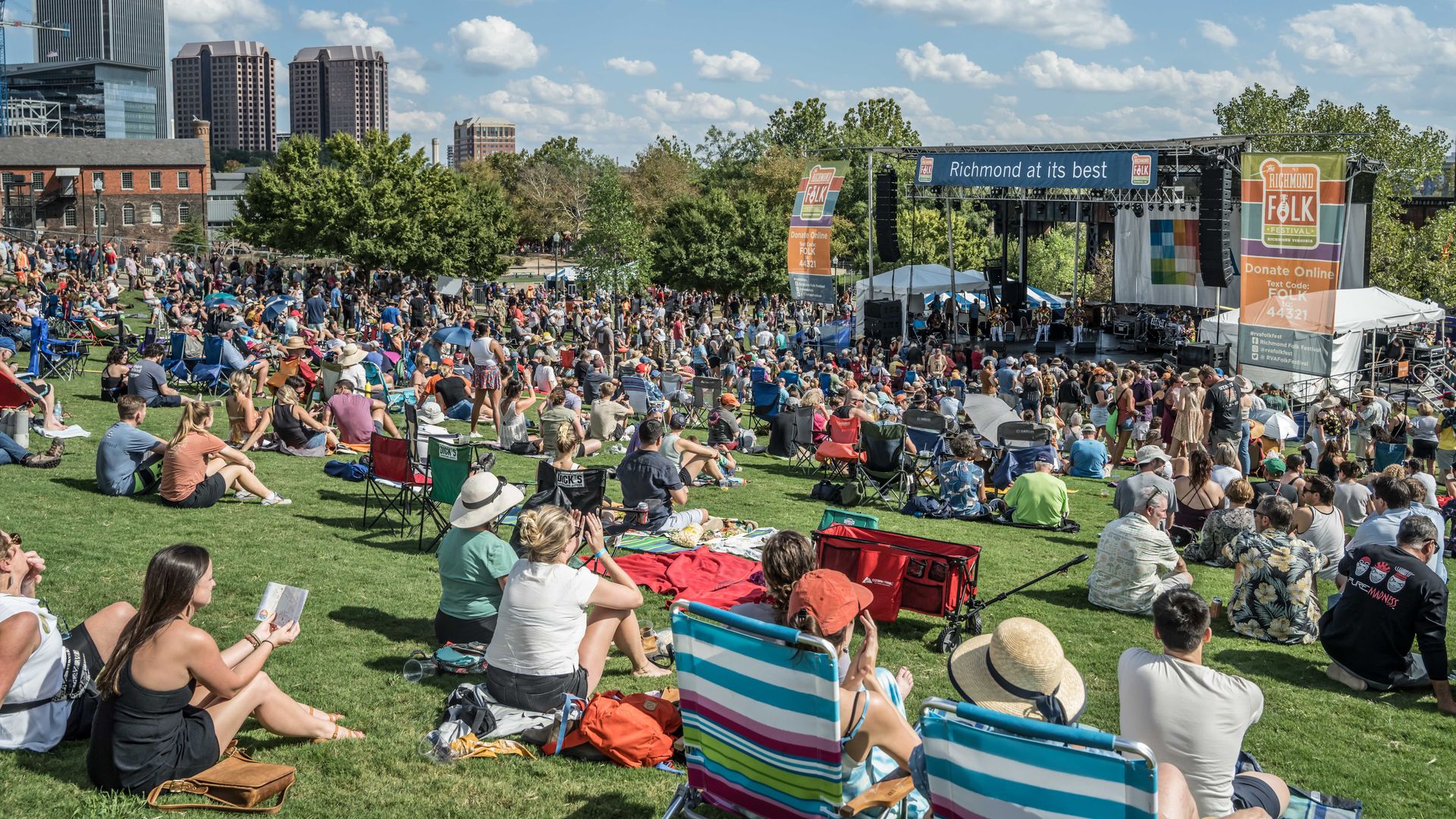 A crowd of people look at a stage with the skyline in the back 