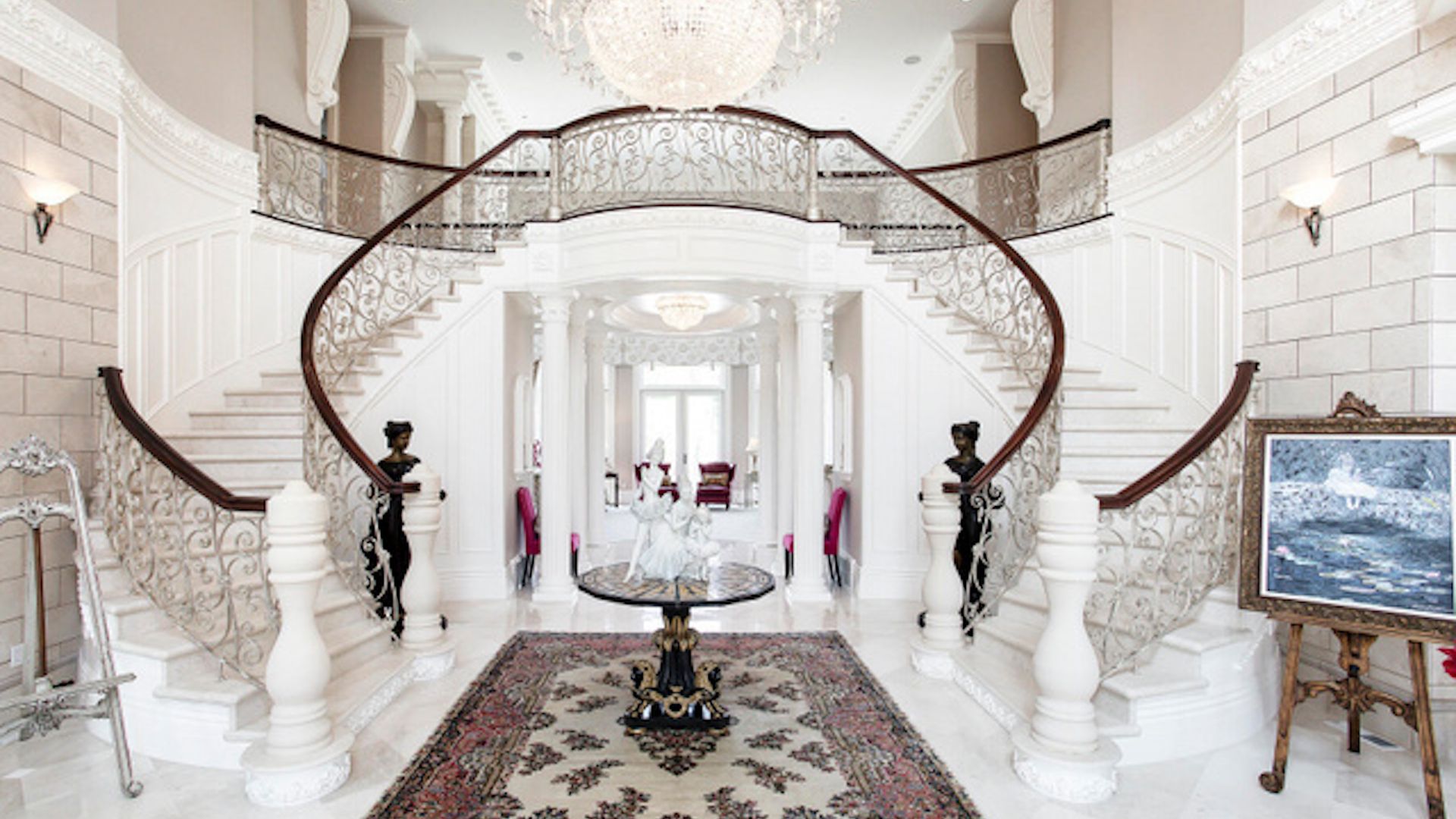 Two staircases wrap around a grand entryway, with a chandelier hanging from the ceiling.
