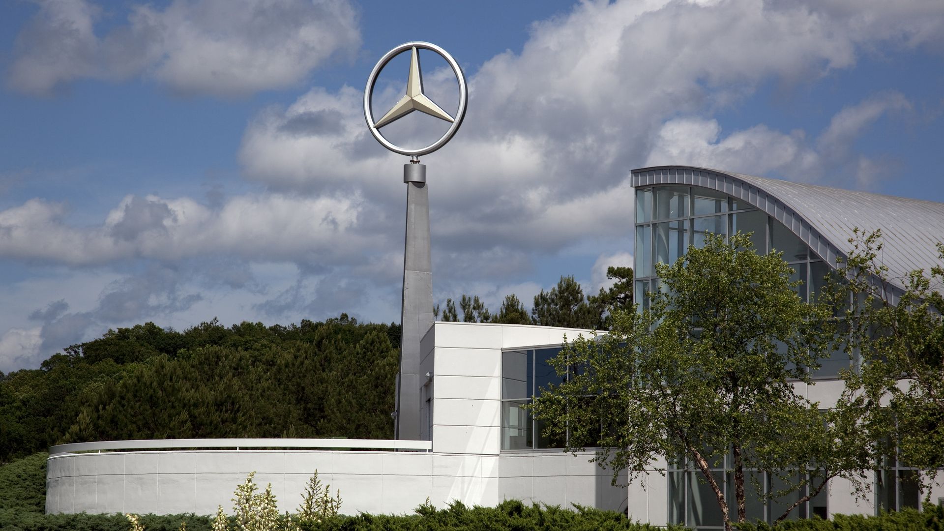 A Mercedes-Benz logo stands on a tall steel pole at a factory