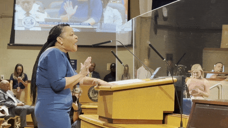 Mayor LaToya Cantrell wears a blue dress and talks behind a podium.