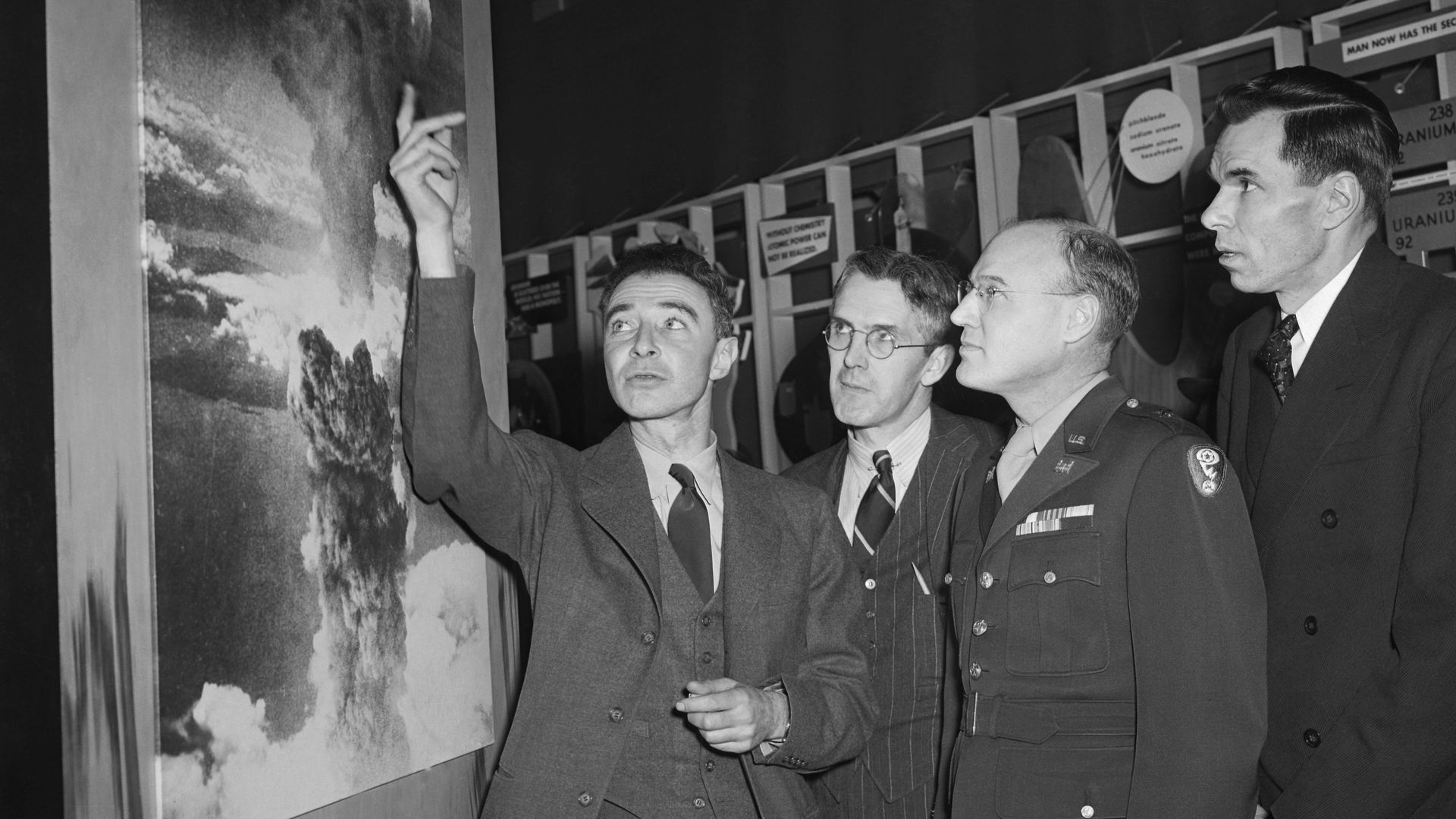 Man pointing to a poster of a bomb while three other men look on.