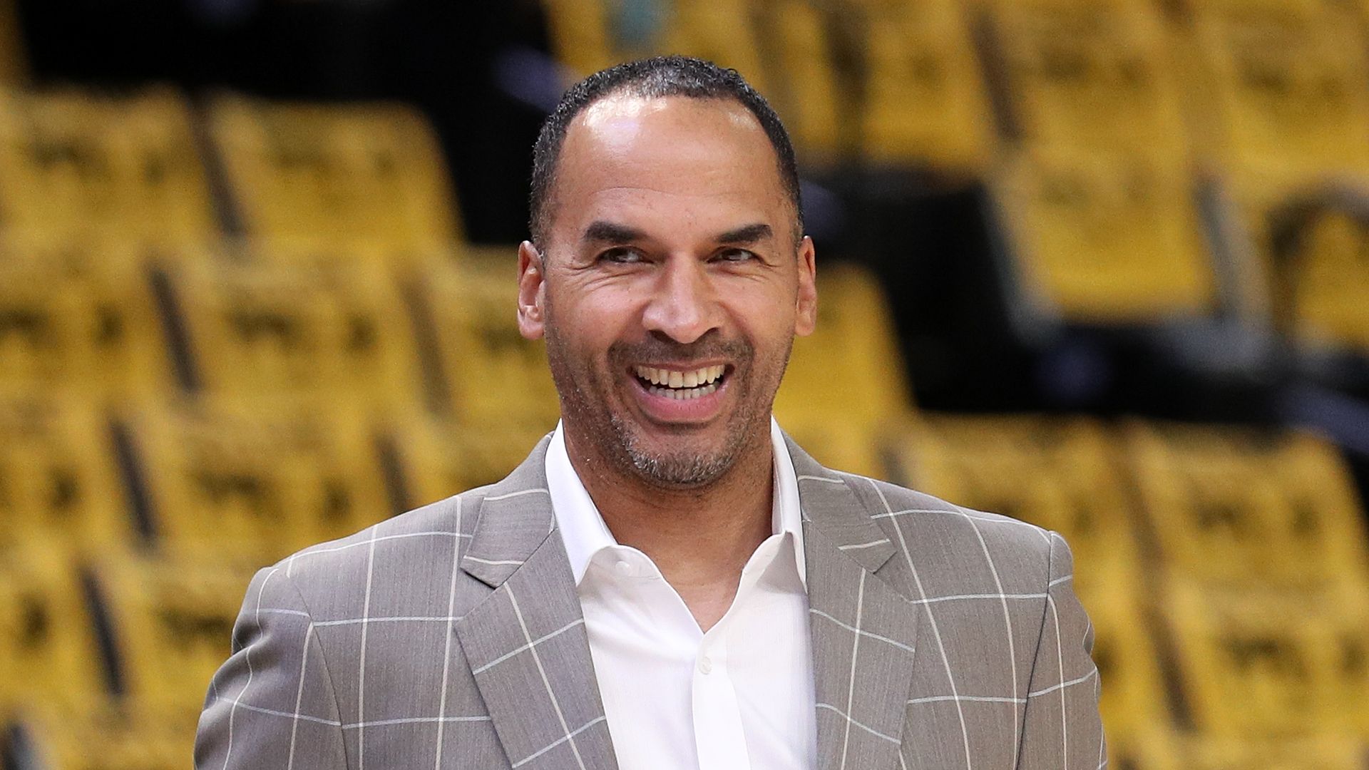 A man smiles while wearing a light brown plaid suit 