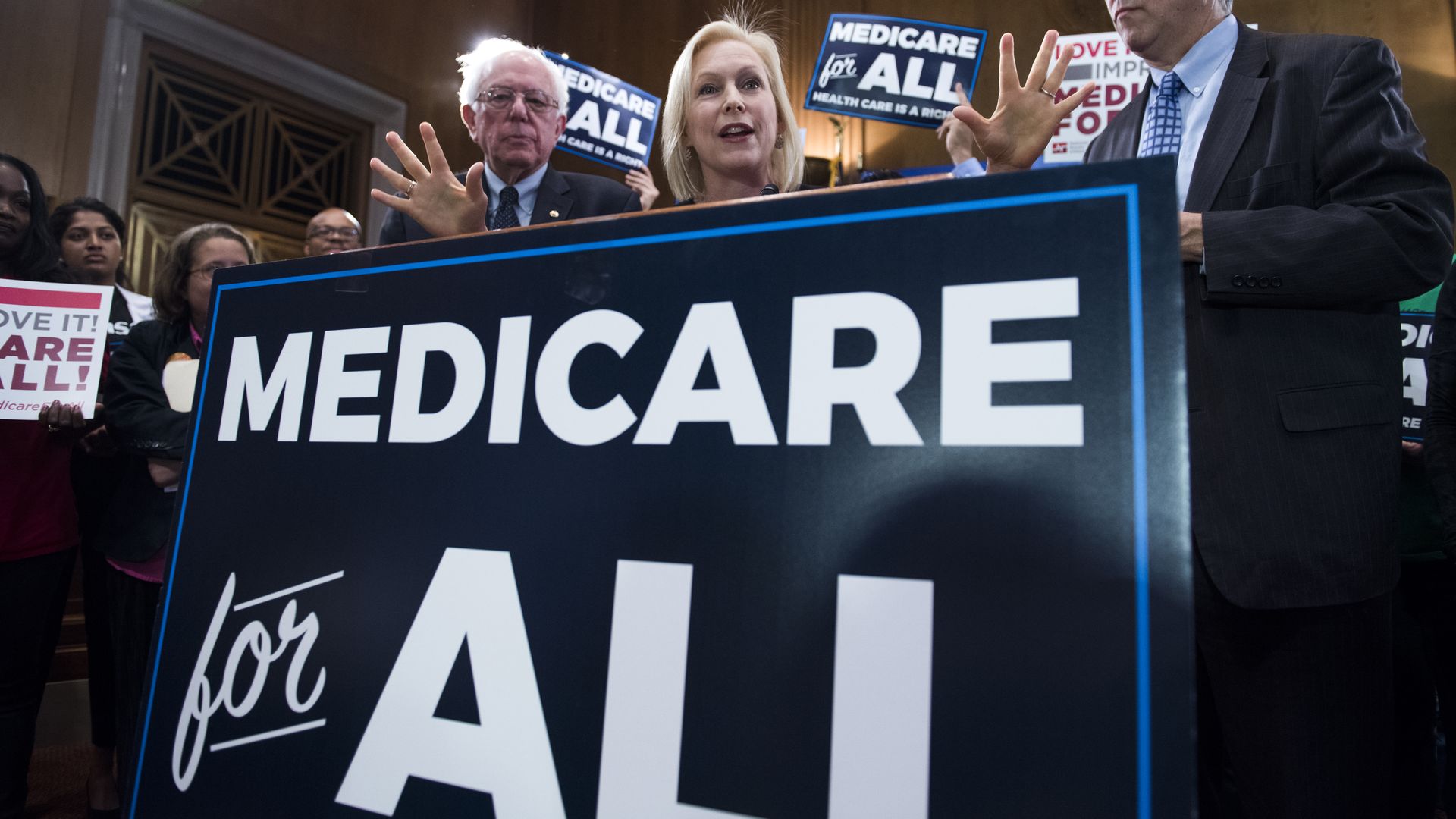 Kirsten Gillibrand ans Bernie Sanders standing behind a medicare for all sign