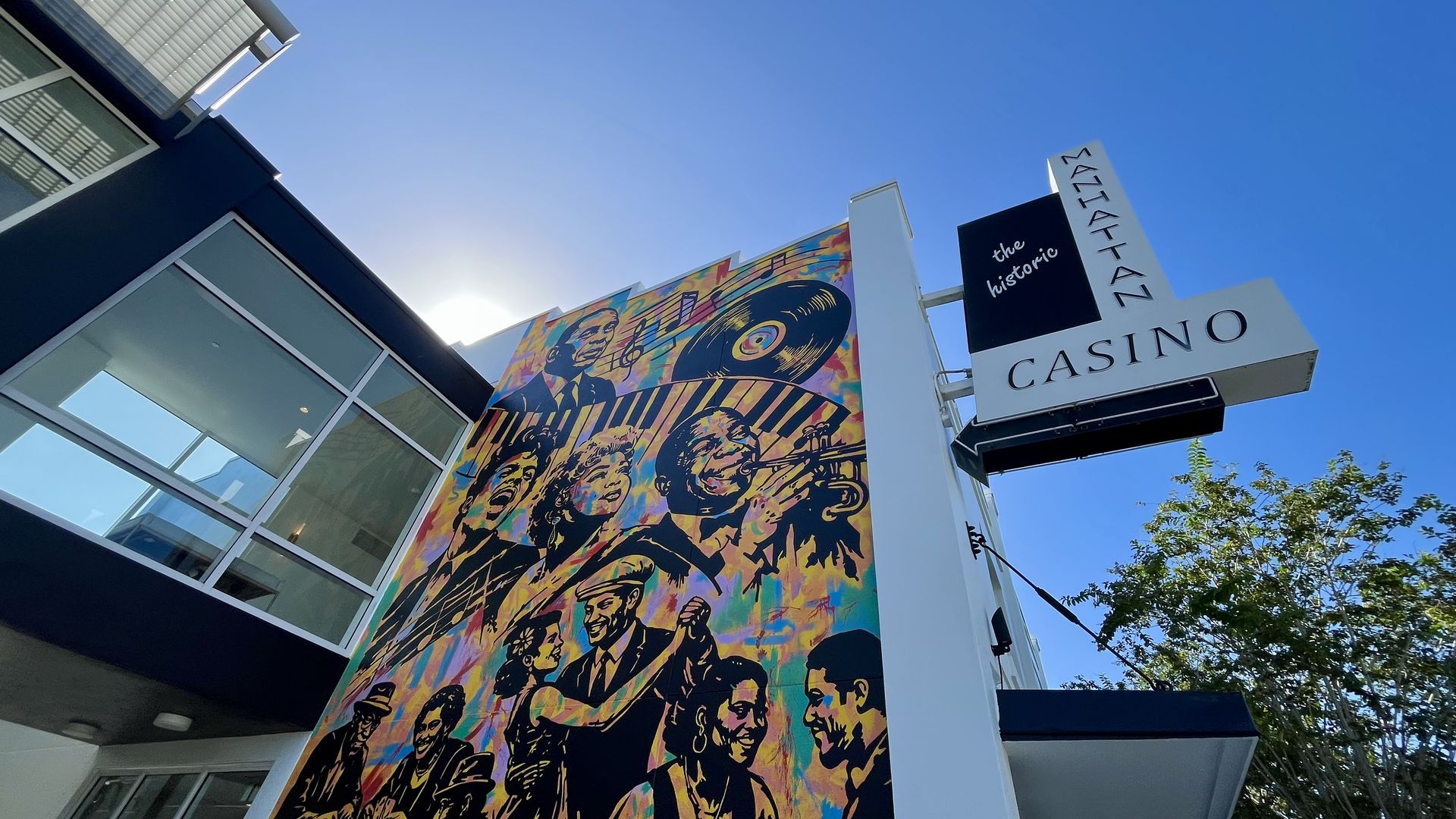 Modern building with glass walls and a large, vibrant mural of jazz musicians and a vinyl record. A white sign reads the historic casino beside it under a clear blue sky.