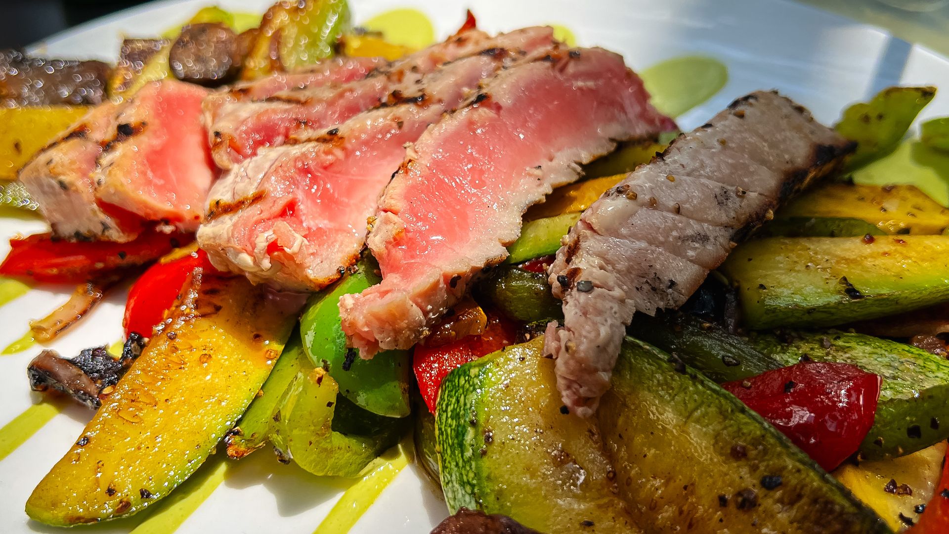 A rare tuna steak on a bed of green, seared vegetables.
