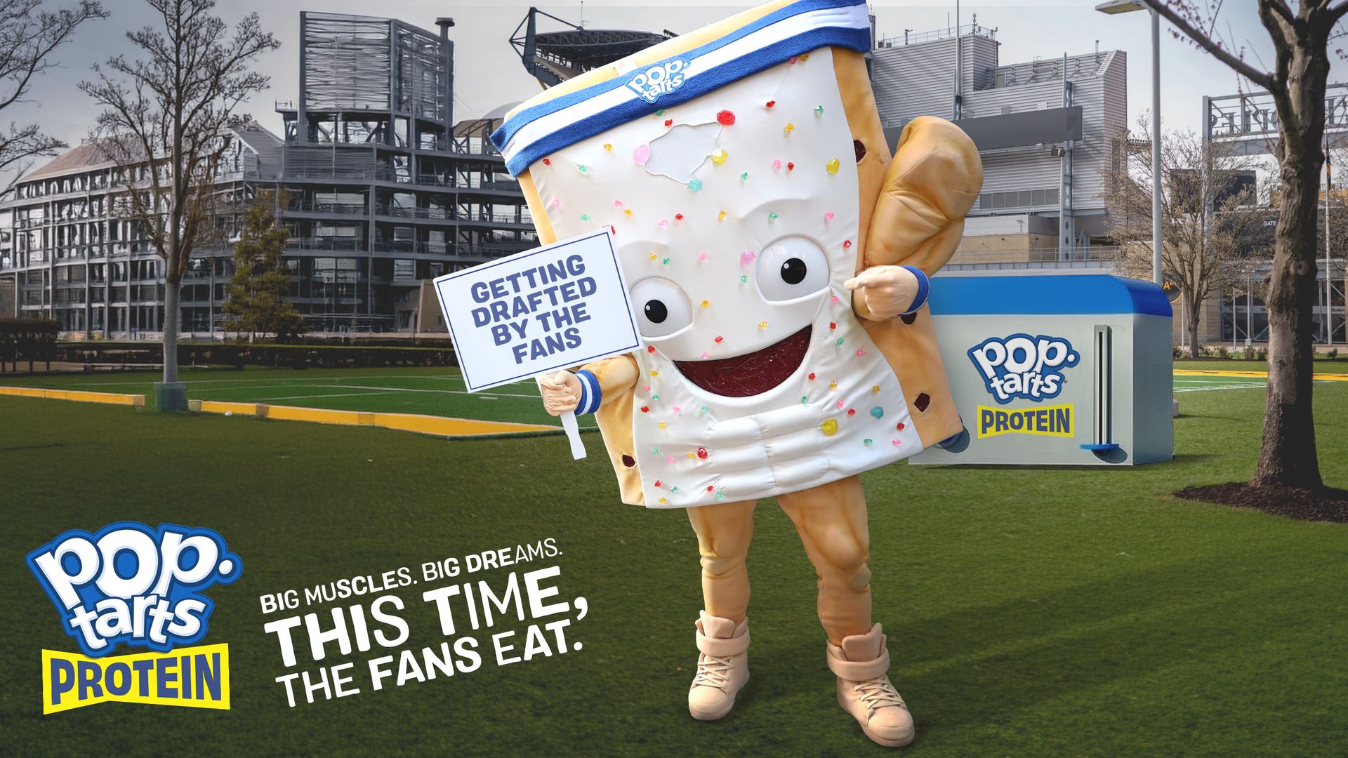 Costumed Pop-Tarts Pastry mascot in a blue-and-white headband with sprinkles, on a grassy field, holding a sign "GETTING DRAFTED BY THE FANS." A large Pop-Tarts Protein box is in the background.