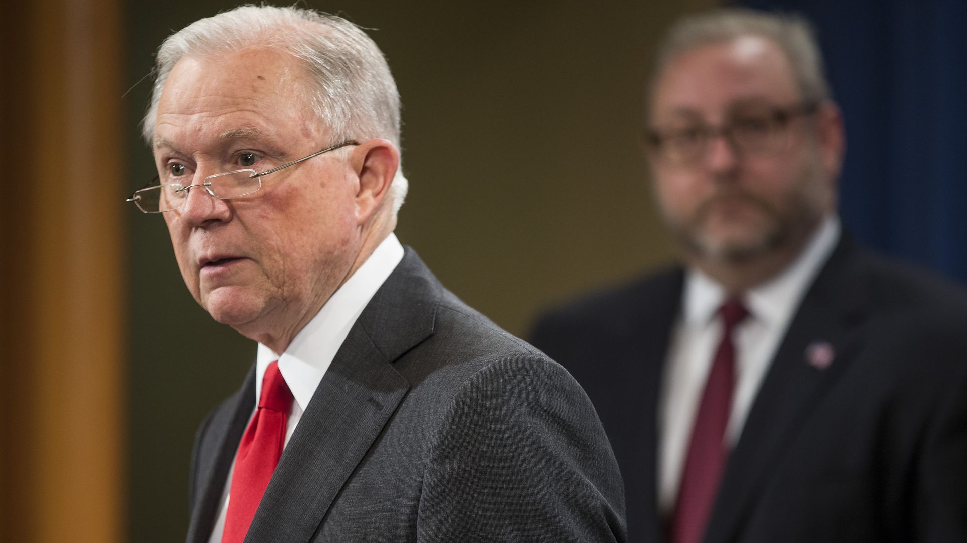 In this image, Jeff Sessions faces the left. He's wearing a red tie and a suit. 