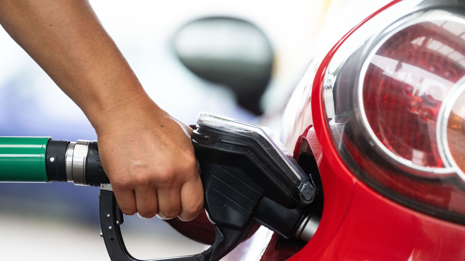 A person squeezes the handle of a gas pump while filling a red car. 
