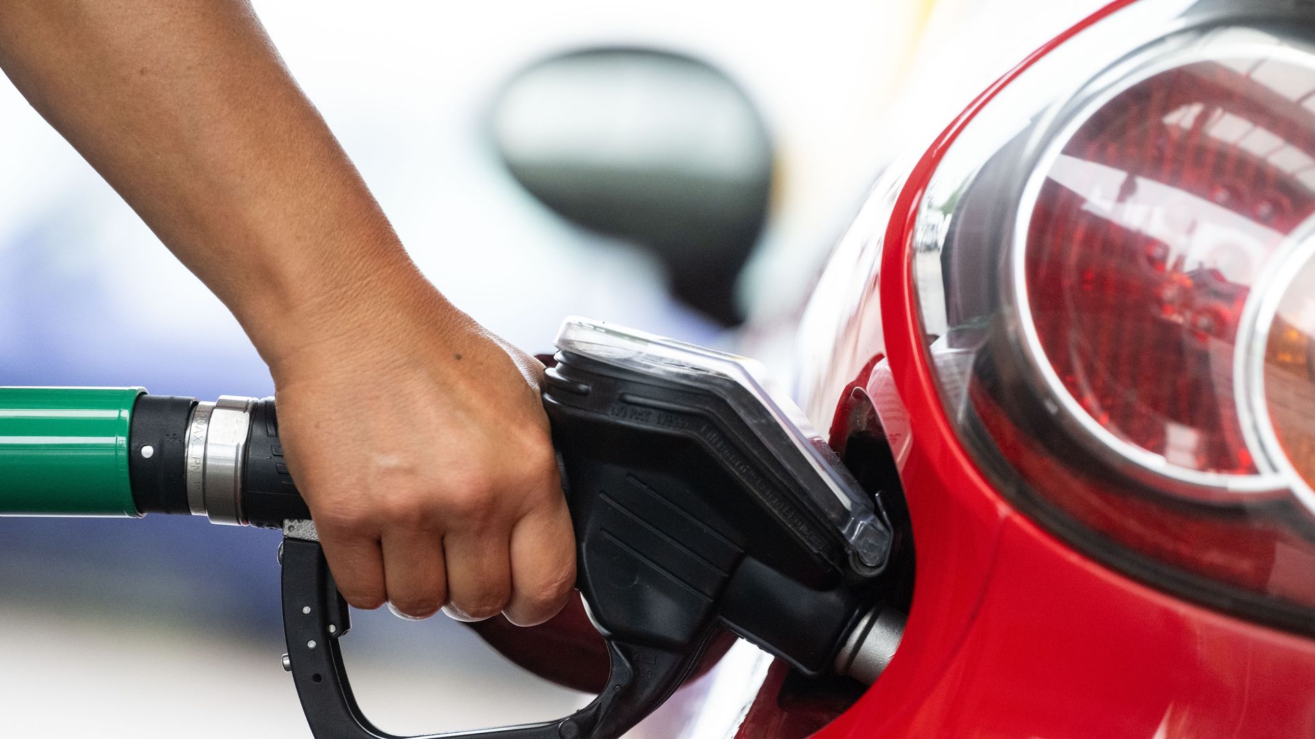 A person squeezes the handle of a gas pump while filling a red car.