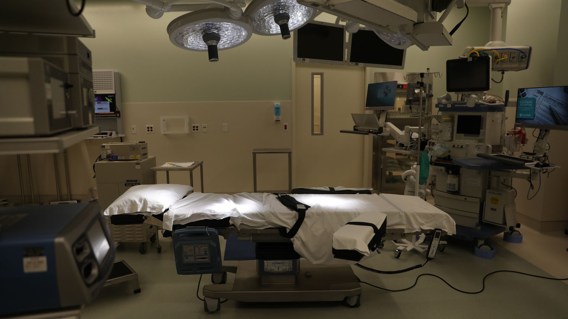 An operating room bed with lights, computers, equipment and devices surrounding it.