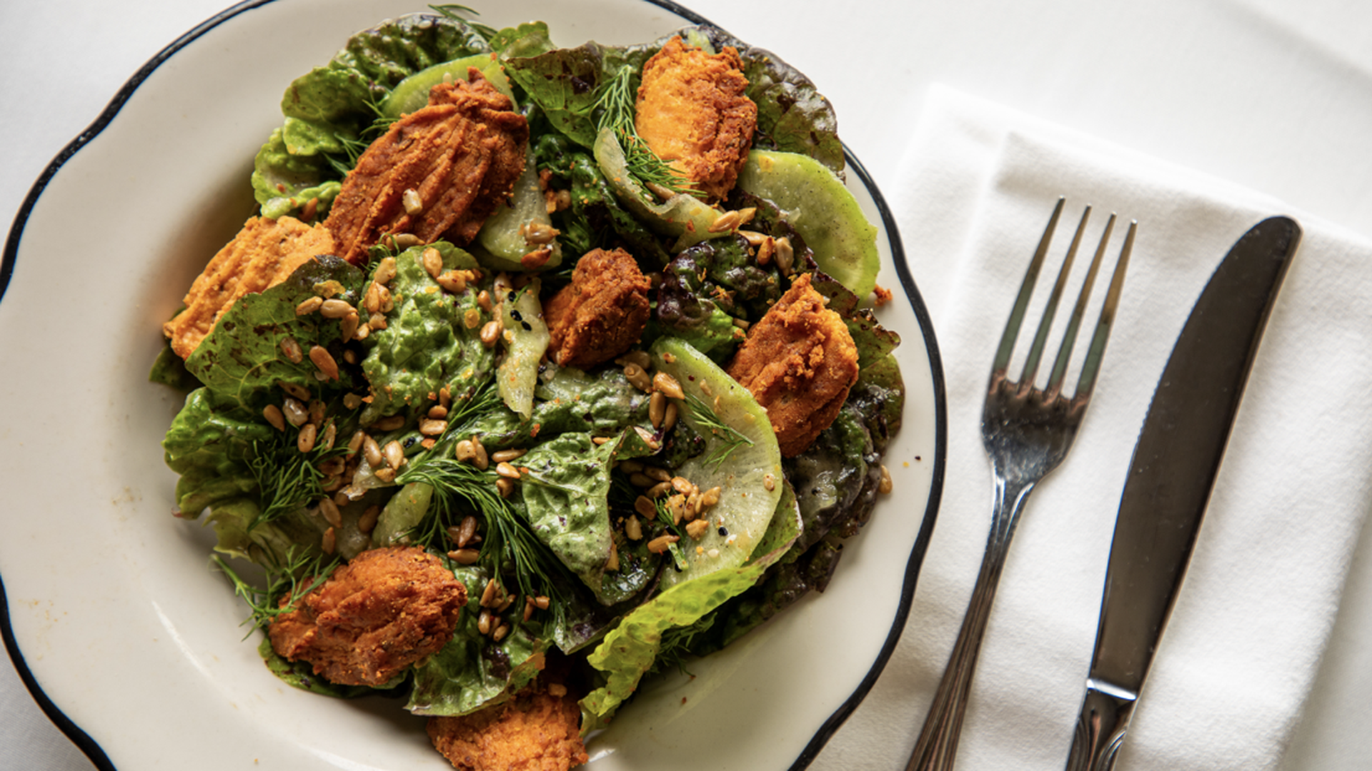 Three-panel image: left shows a wooden wine cabinet with bottles and a floral arrangement; center features a green salad with croquettes on a white plate; right depicts a chef in a blue apron outdoors.