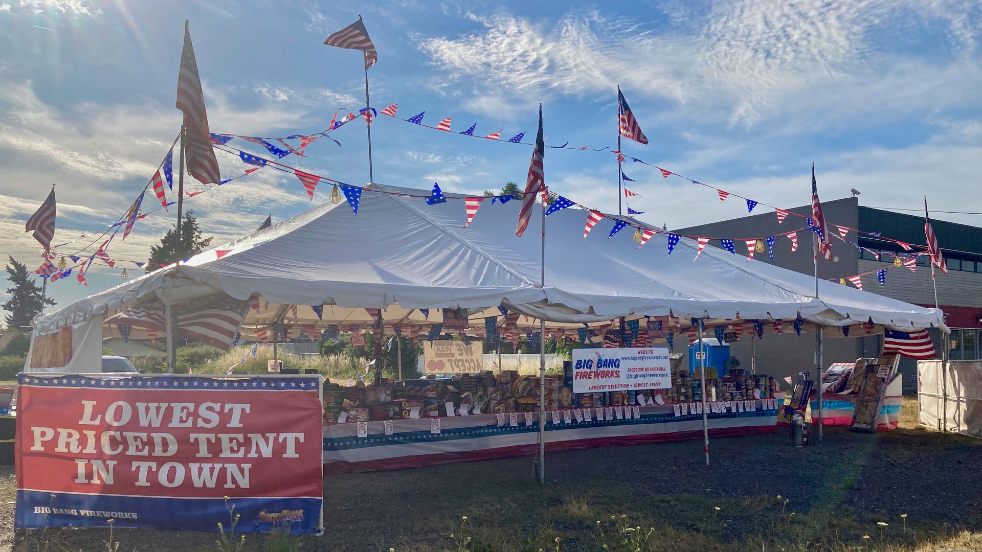 A white tent decorated with American flags and bunting, with a big red sign that says lowest priced tent in town.