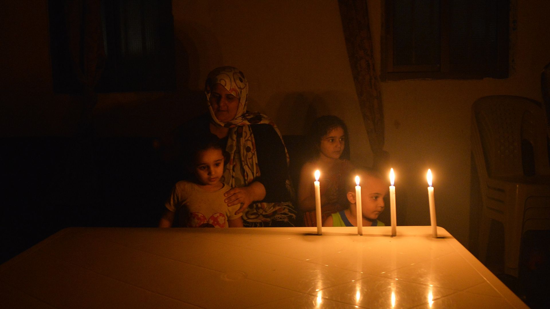 Photo of an adult and two children sitting at a table in the dark with four candles lit on the table