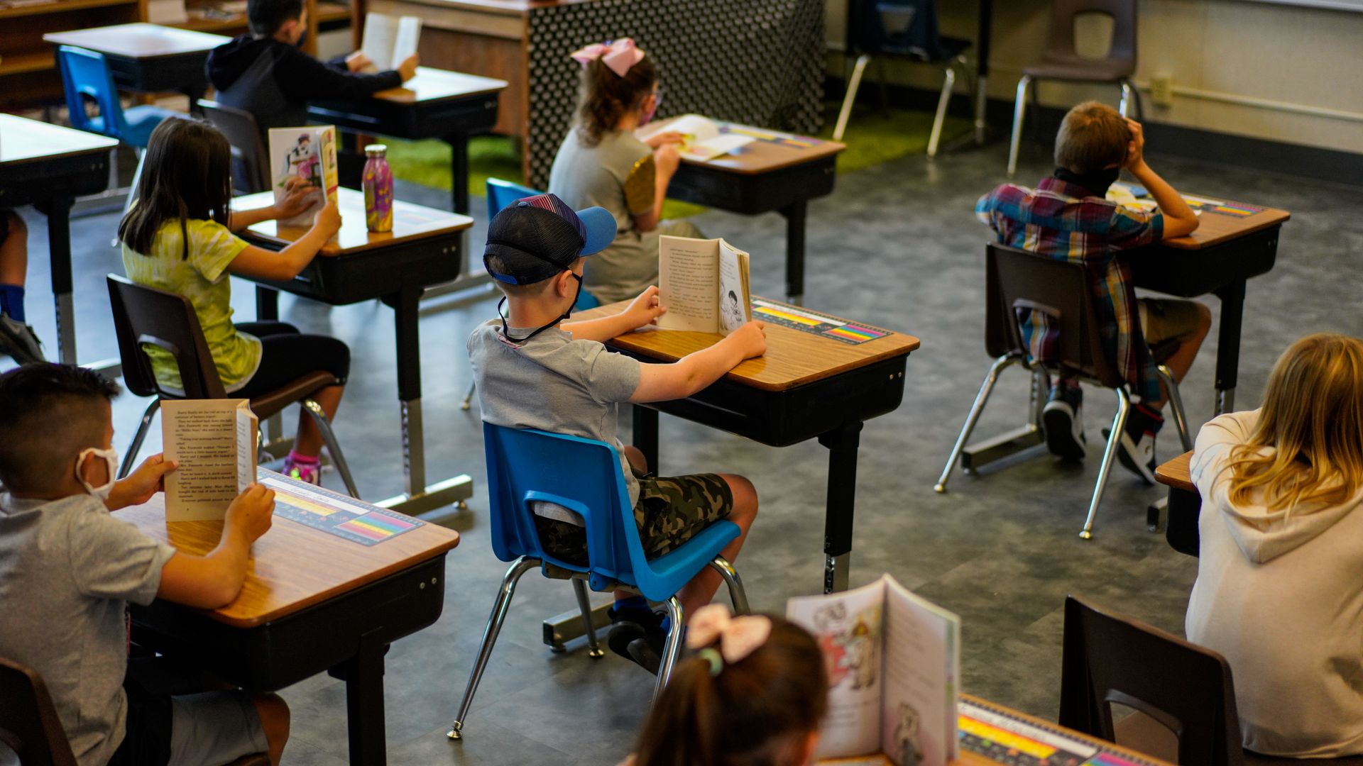 Children in class reading books at socially distanced seats.