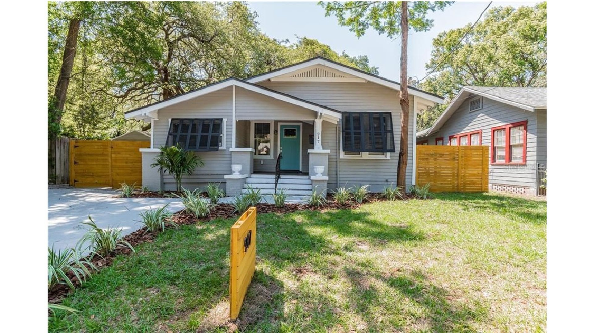 A photograph of a well-kept grey craftsman bungalow house with white trim and a green lawn.