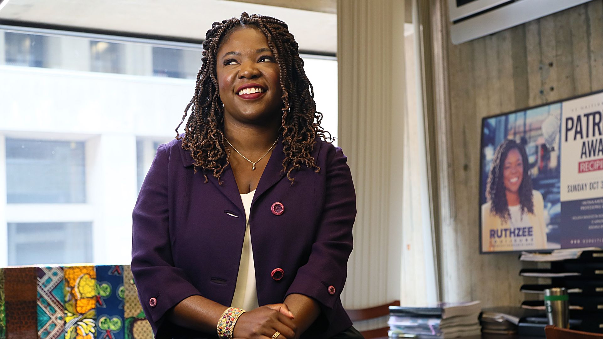 Boston City Council Ruthzee Louijene, who is seeking reelection,  sits on a desk and poses for a photo looking off into the distance