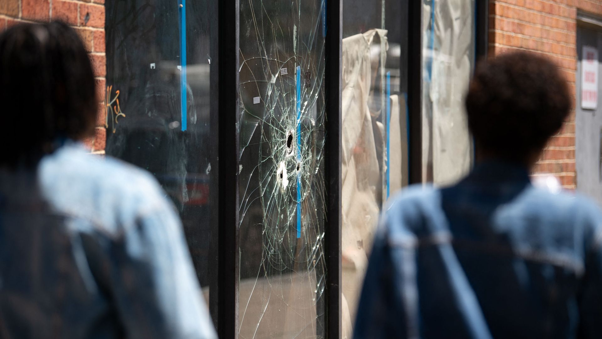 Pedestrians walk past bullet holes in the window of a store front on South Street.