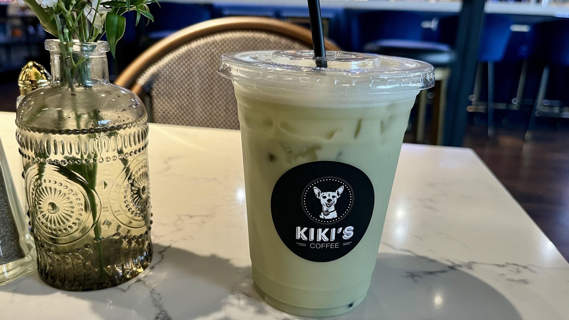 A plastic cup filled with a green liquid sits on a marble tabletop. 