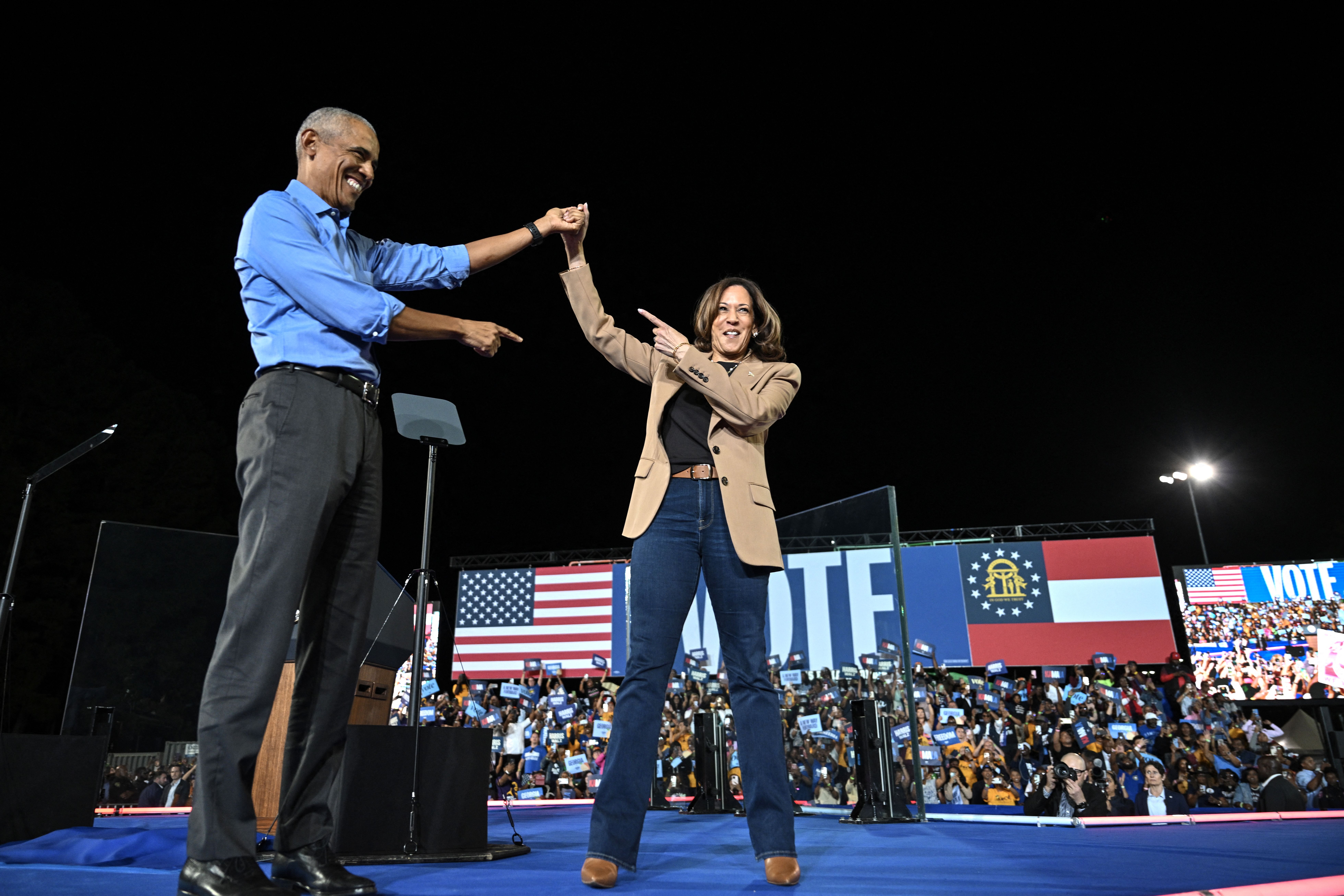 Former US President Barack Obama hold hands with US Vice President and Democratic presidential nominee Kamala Harris during a campaign rally at the James R Hallford Stadium in Clarkston, Georgia