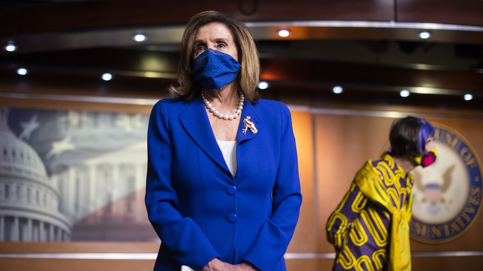 Speaker of the Houes Nancy Pelosi in a press room wearing a matching blue mask and suit