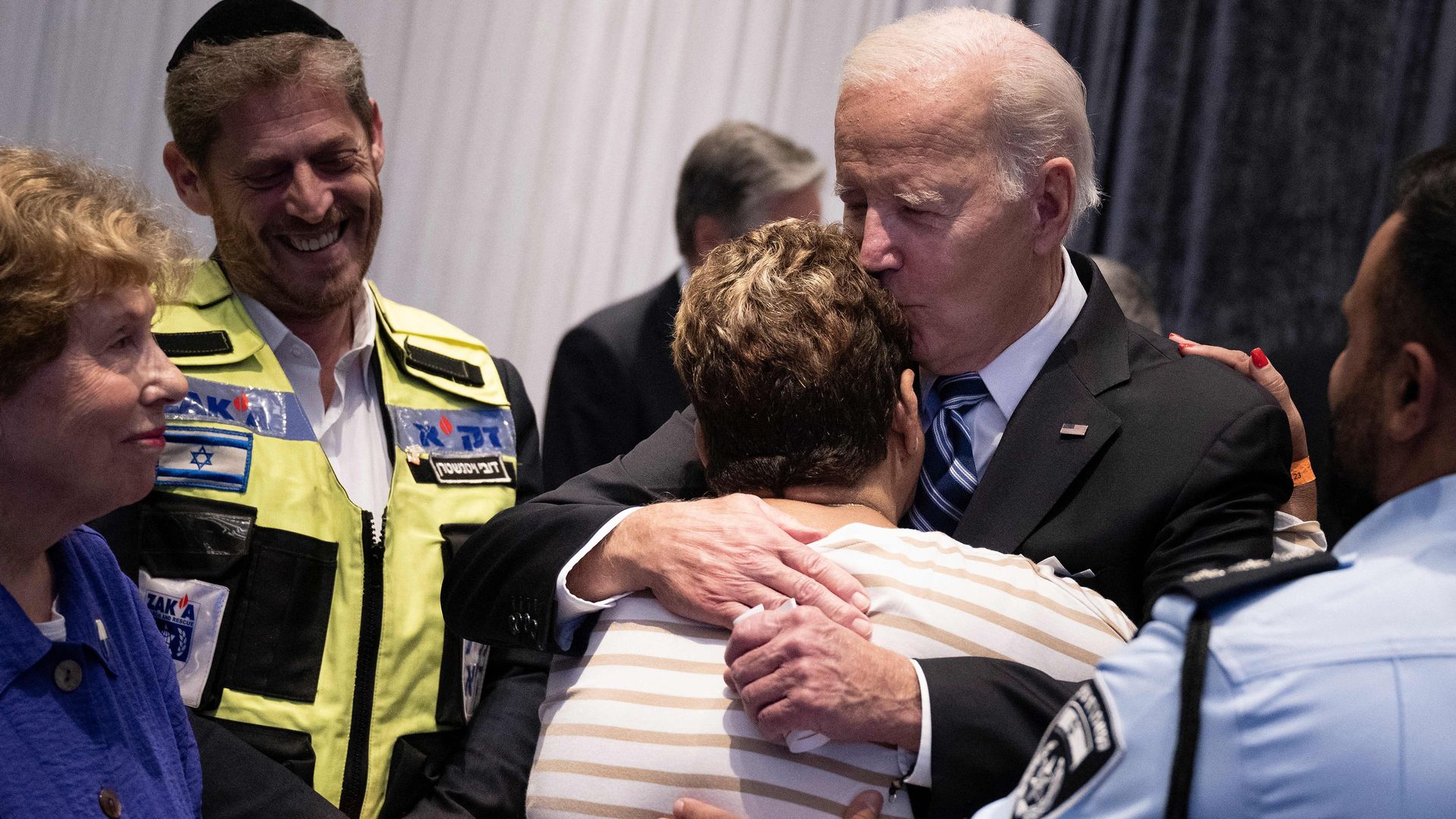 President Biden hugs an Israeli woman in a striped shirt, kissing her on the head.