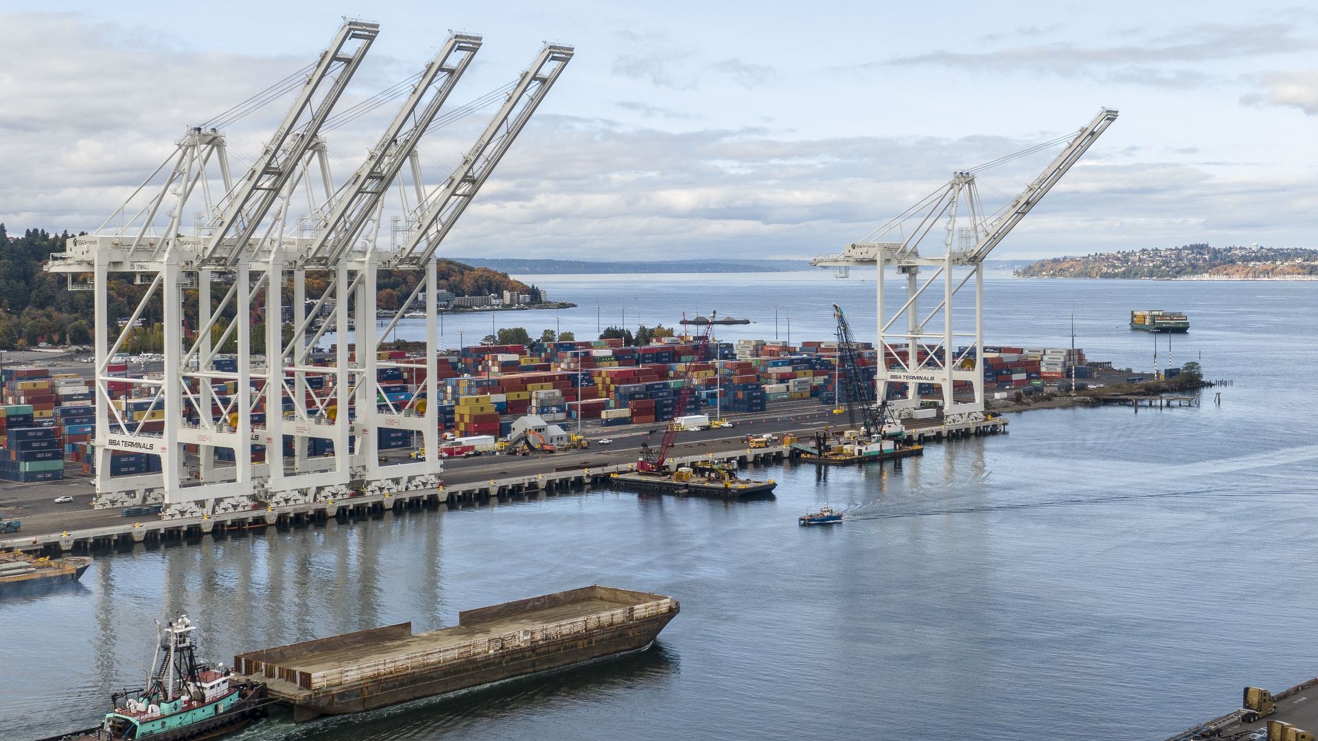 A ship moves through a waterway with white cranes designed to move containers off of boats.