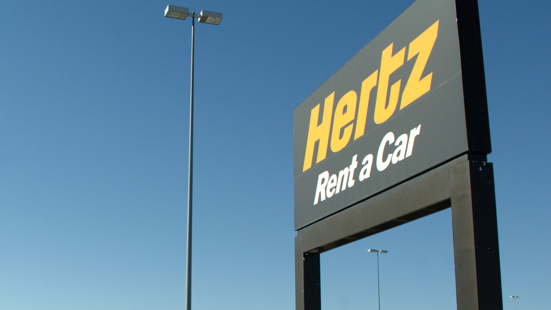 A row of rental cars parked below a sign for Hertz at Denver International Airport. Photo: Matthew Staver/Bloomberg via Getty Images