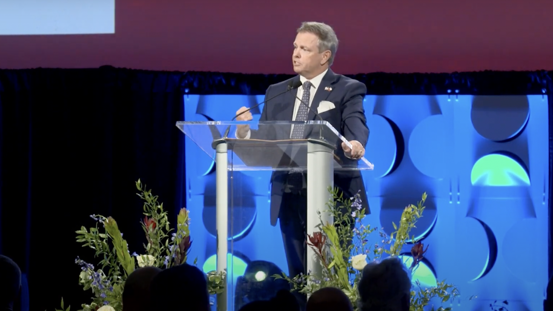 A man stand behind a podium wearing a suit 